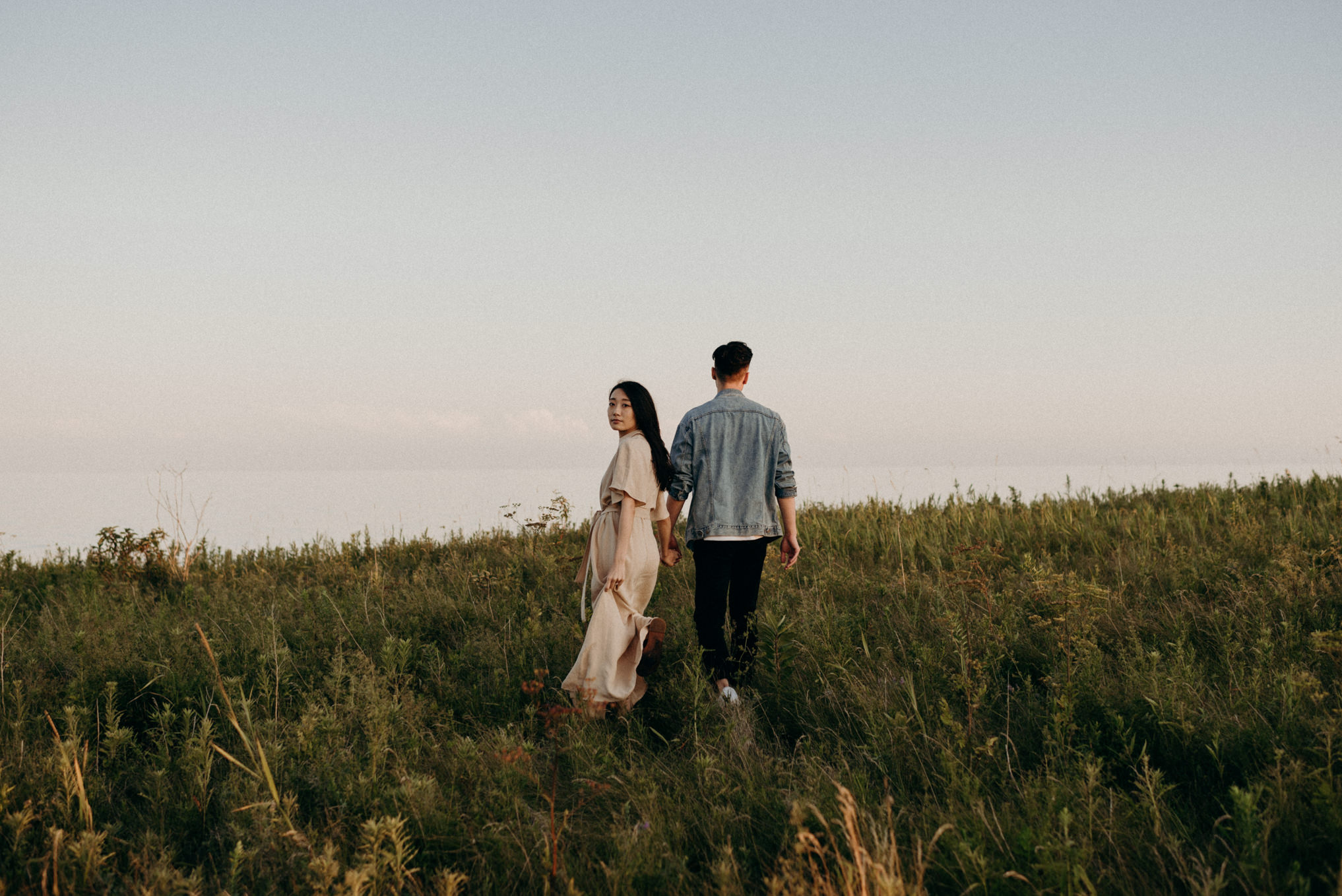 Asian couple walking along cliff edge overlooking water at sunset