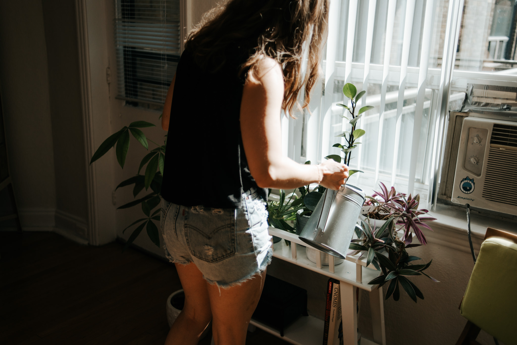 Girl watering plants by window inside apartment