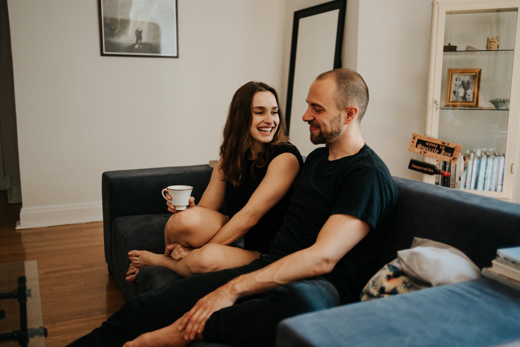 Couple laughing and cuddling on couch while drinking coffee