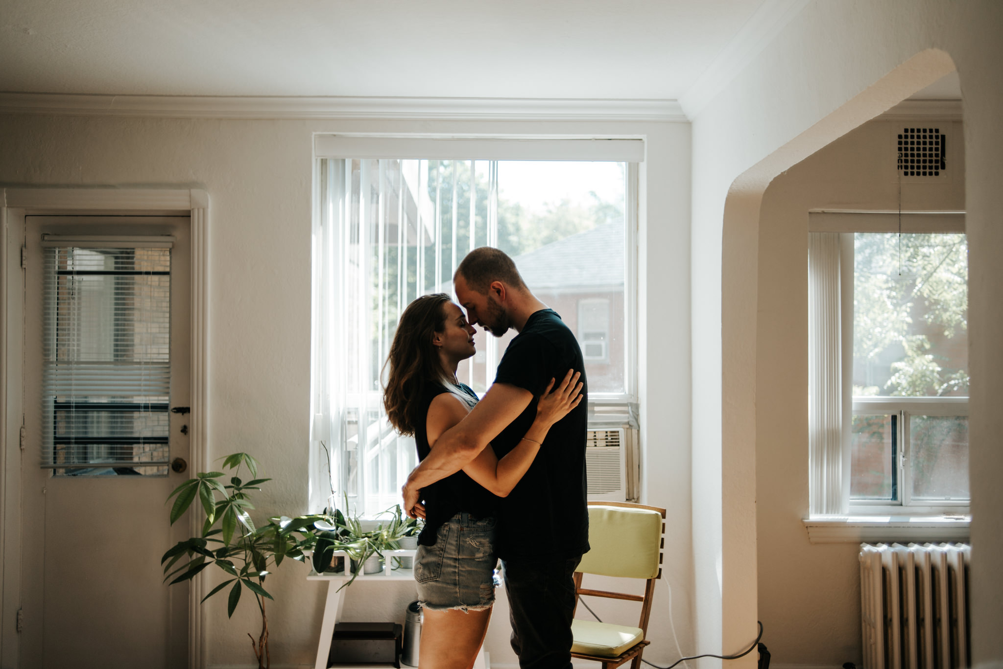 Intimate moment between young couple as they hug by window in living room