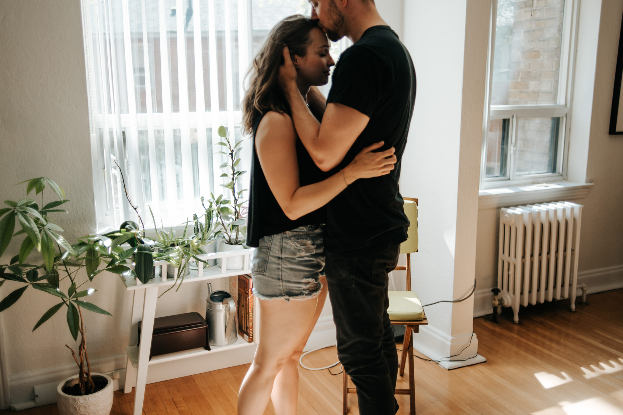 Intimate moment between young couple as they hug by window in living room