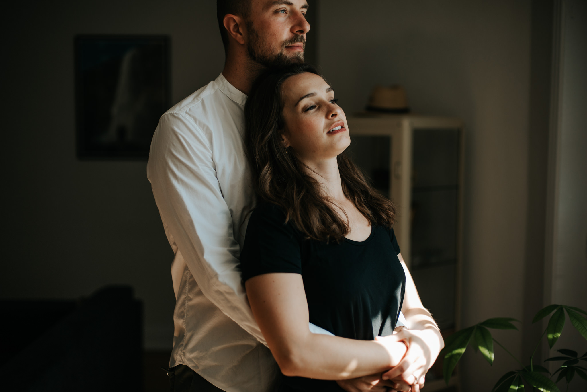 Intimate moment between young couple as they hug by window in living room