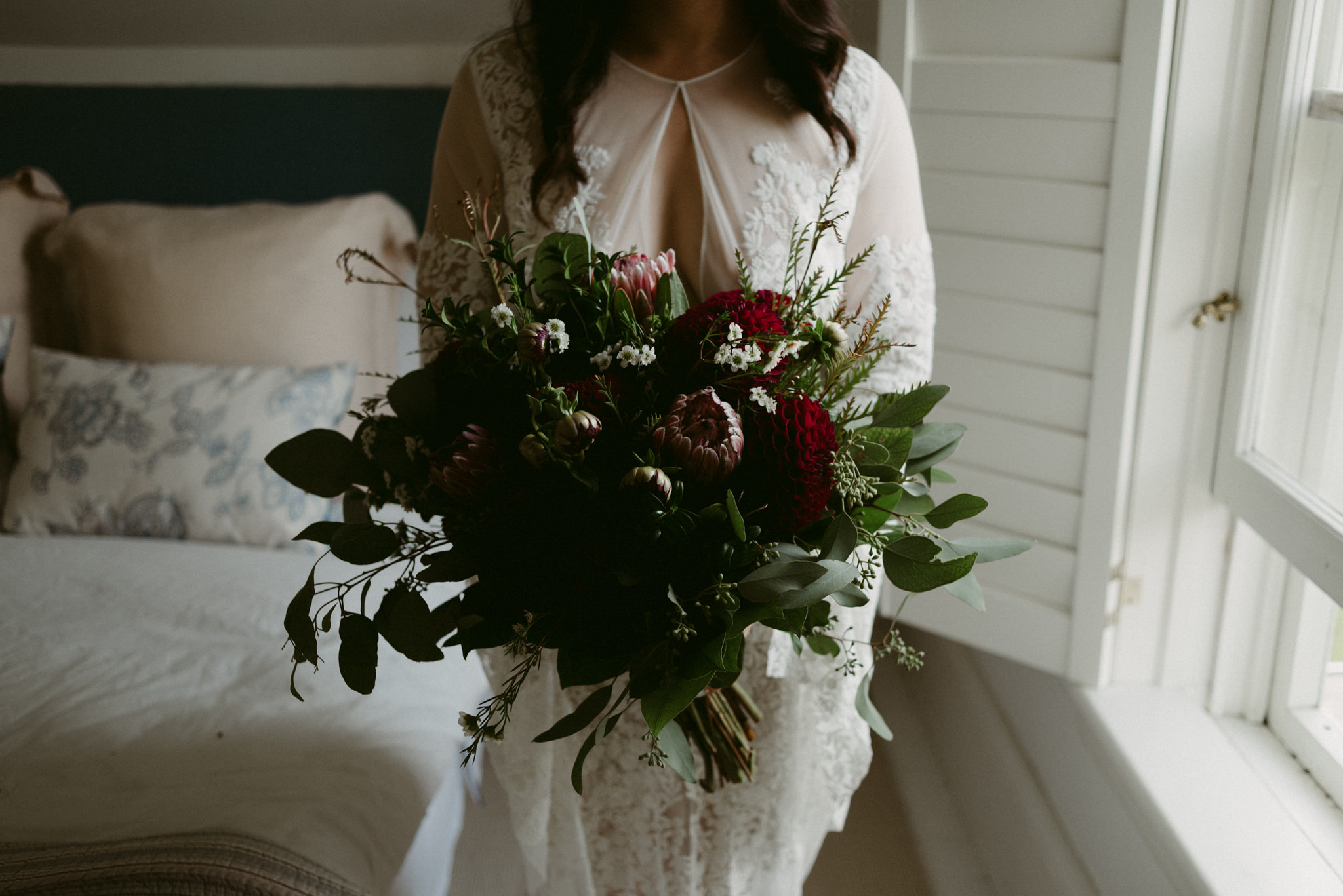 Bride in lace dress holding maroon and dark green bouquet
