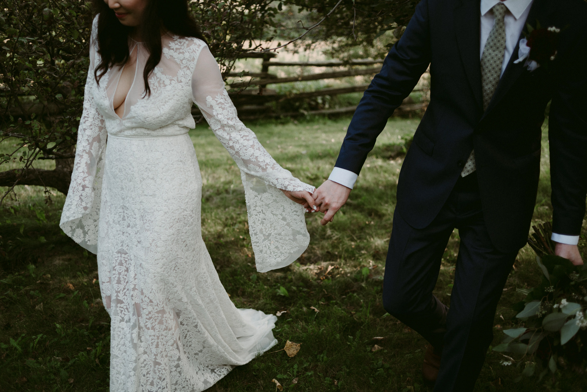 bride and groom walking hand in hand in orchard