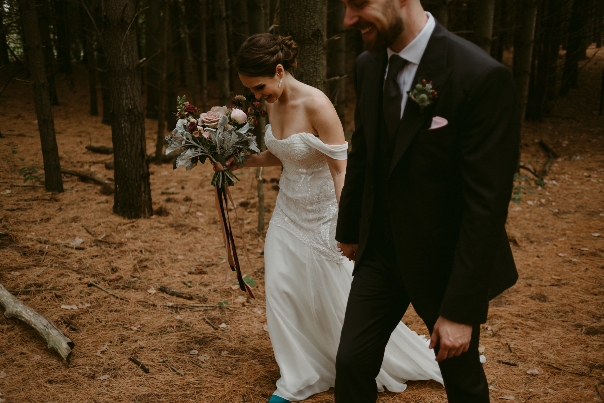 Bride and groom holding hands, laughing and walking in forest