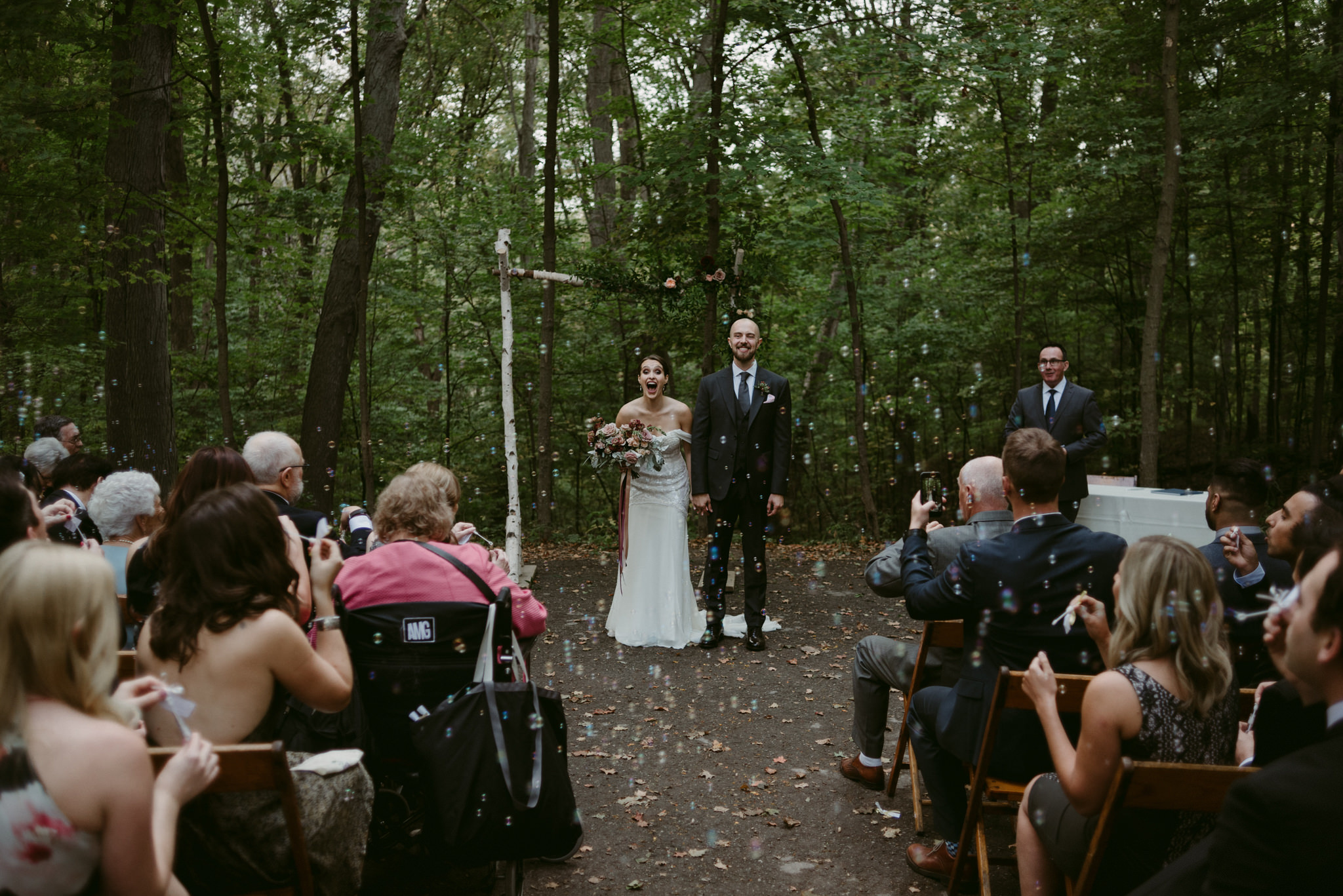 Bride surprised as guests blow bubbles at wedding ceremony