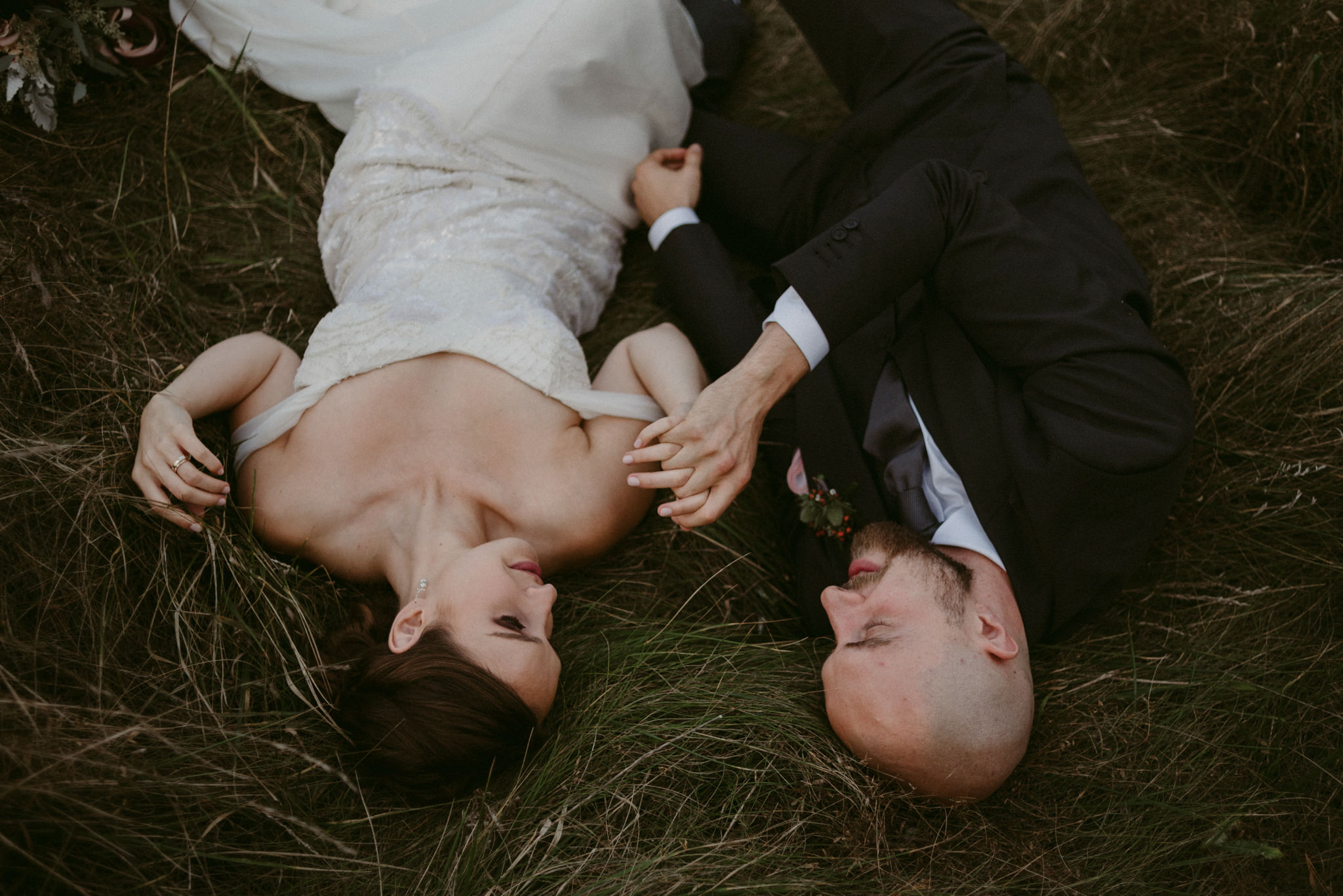 Bride and groom lying down side by side in field