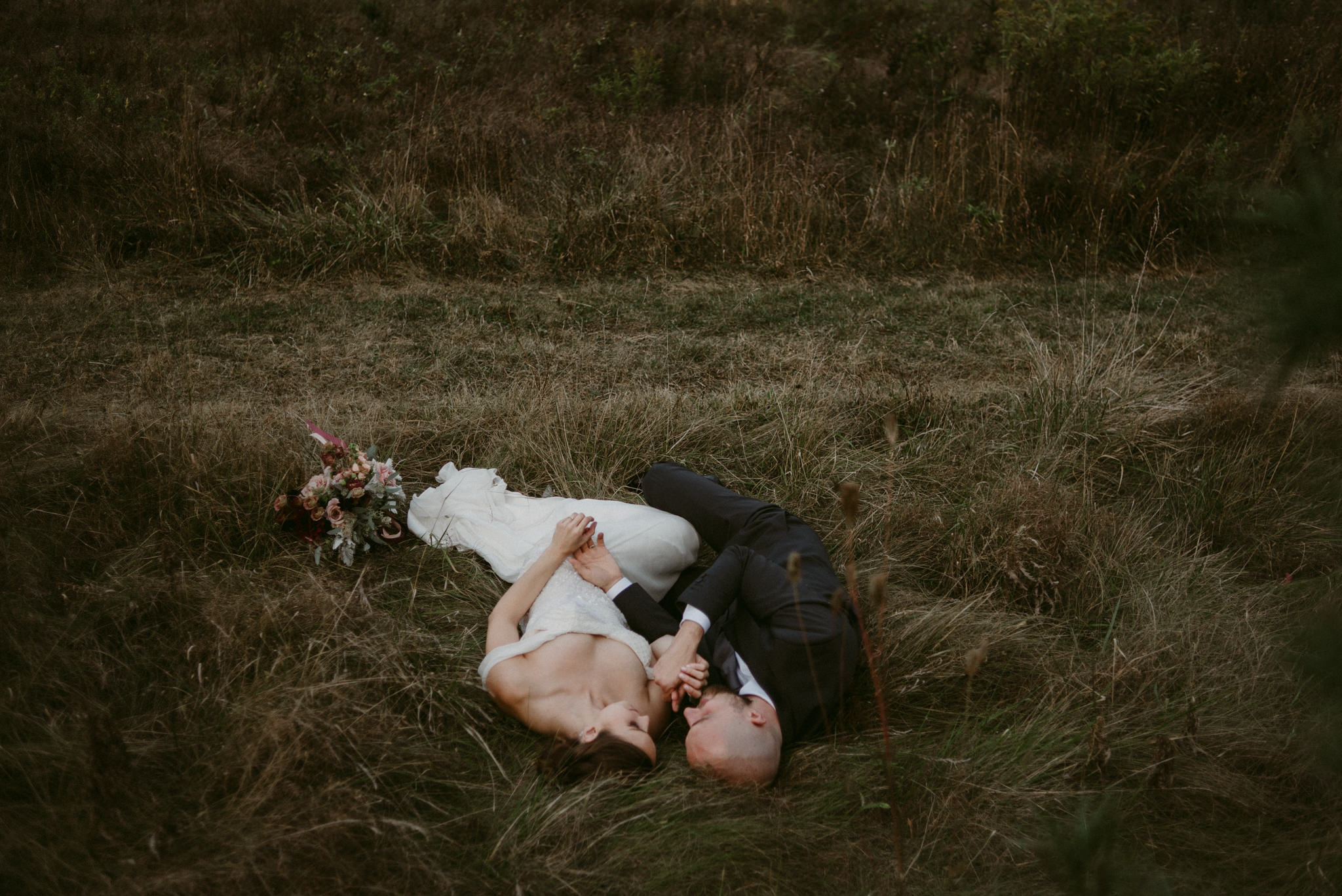 Bride and groom lying down side by side in field