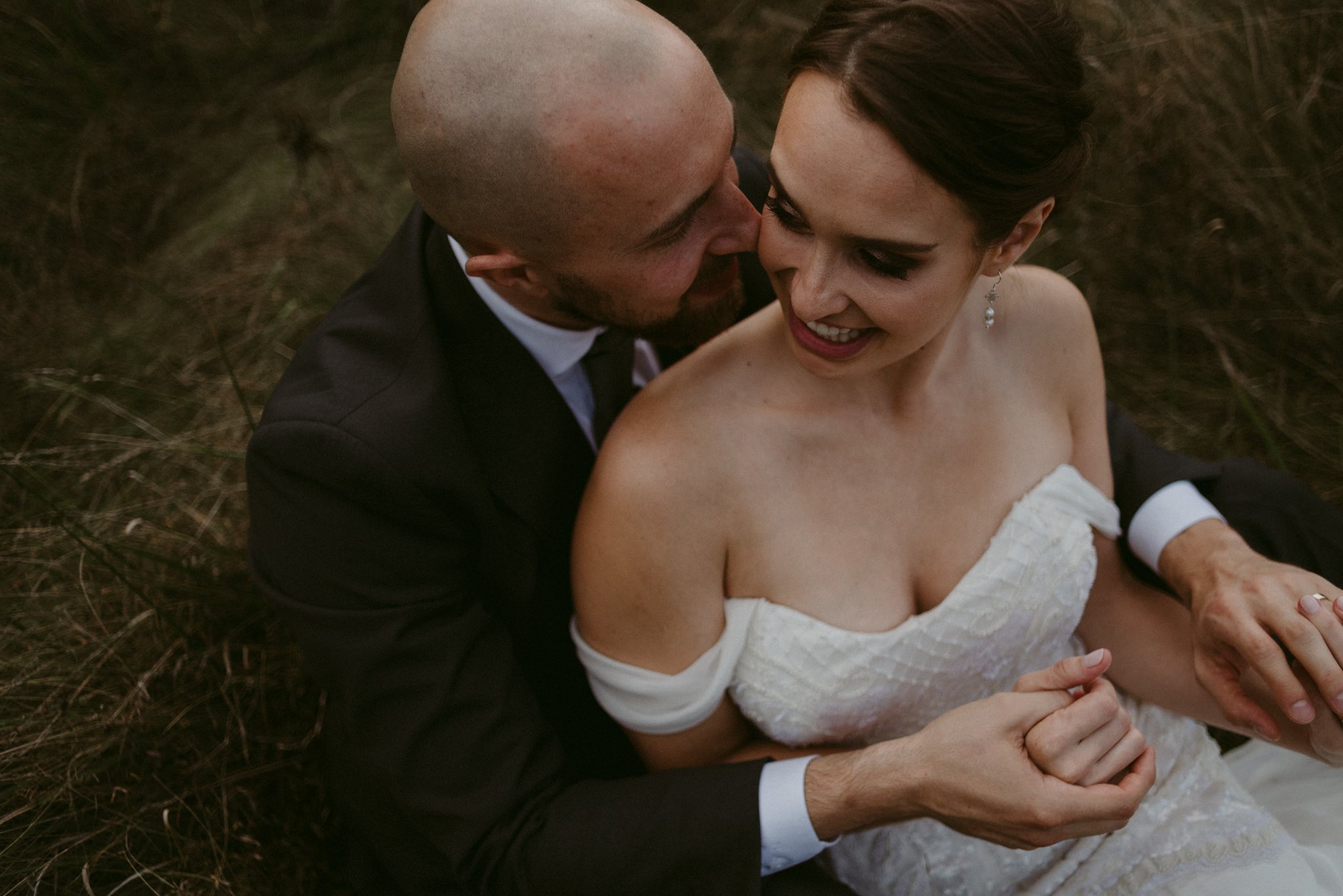 Bride cuddling into groom in field