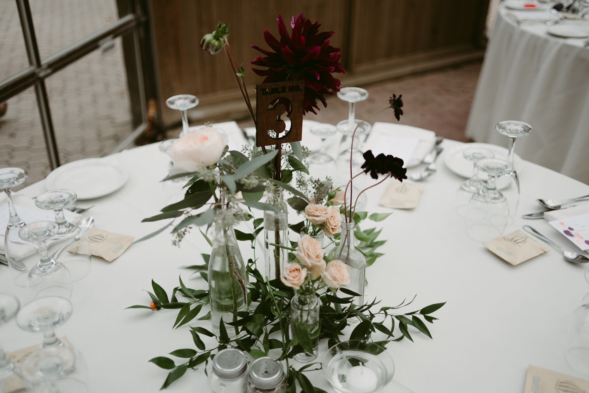 Flower and greenery centrepieces for wedding reception with wooden table number