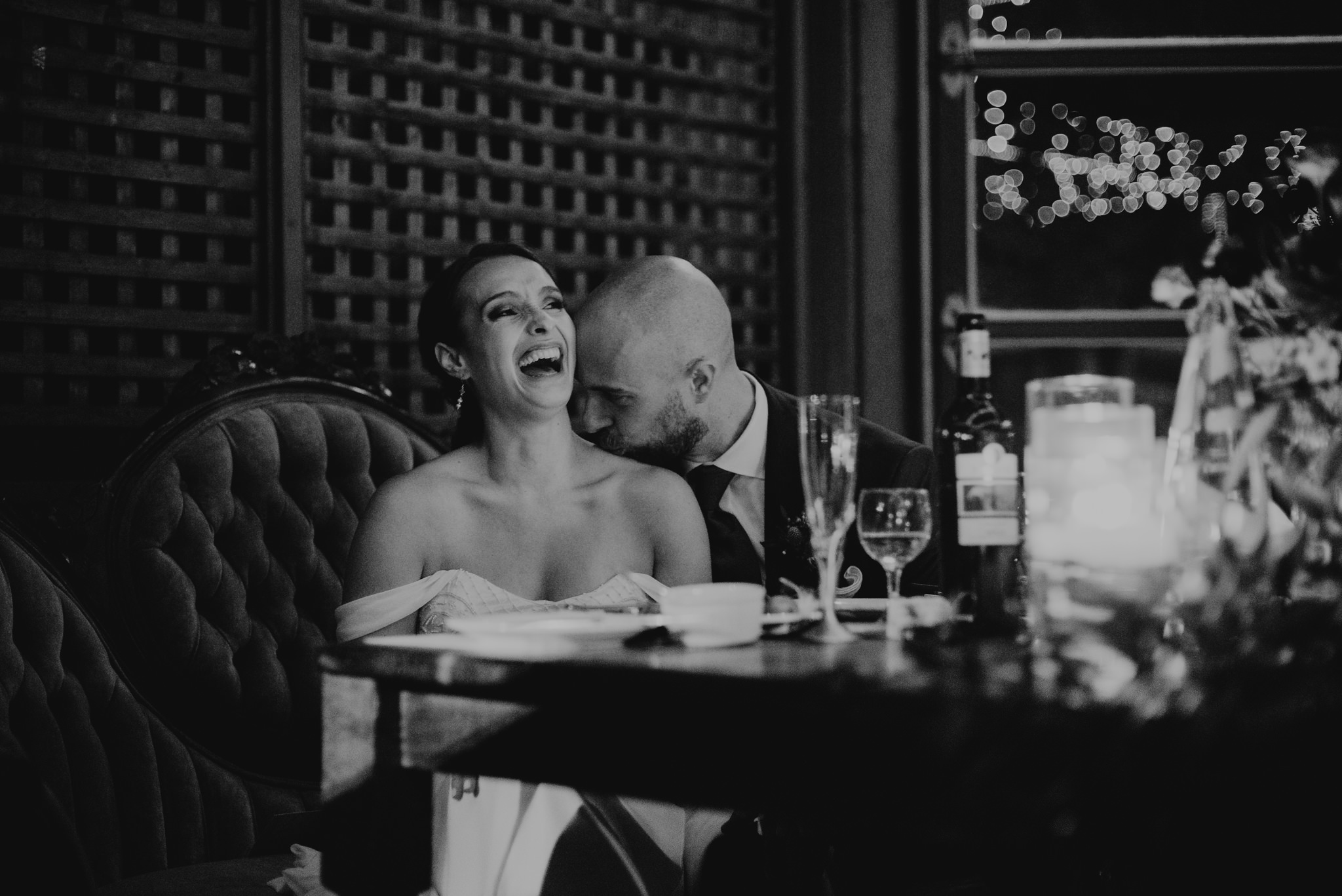 bride laughing and groom kissing bride's shoulder during speeches at wedding