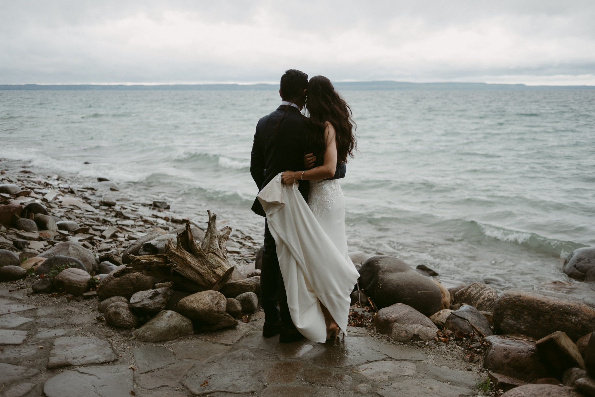 Bride and groom hugging and looking out onto water