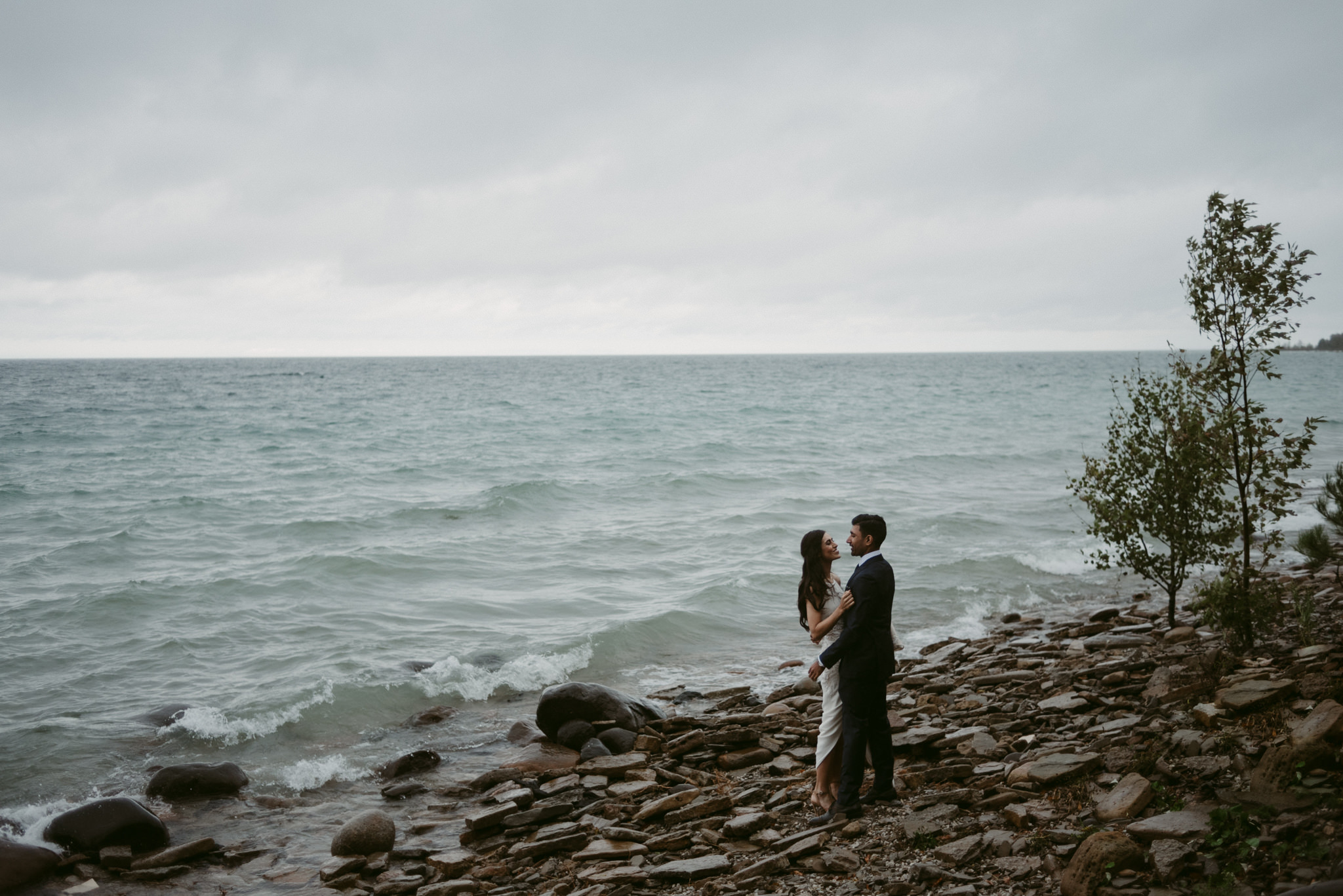 Bride and groom hugging on lakefront on stormy day