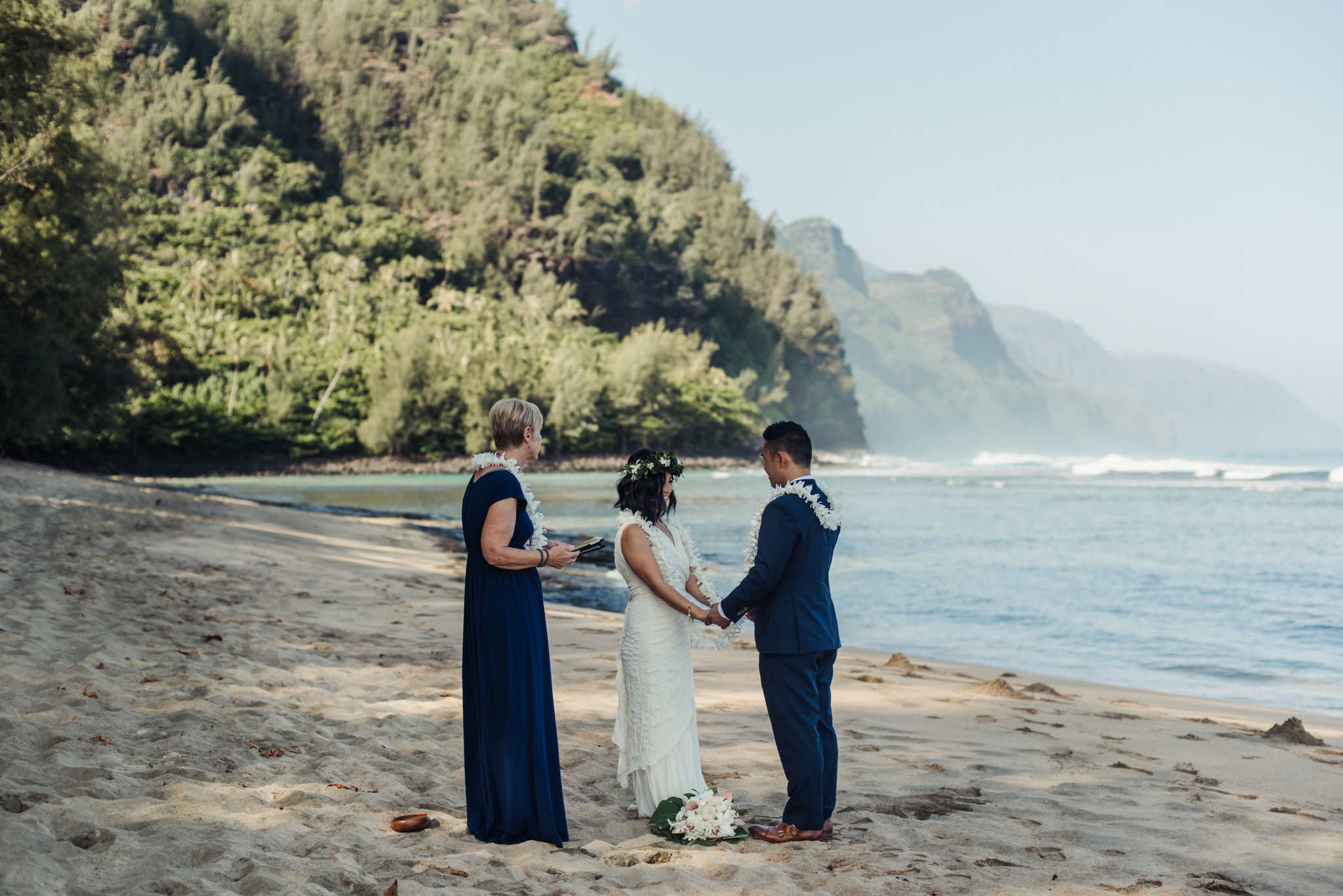 Bride and groom holding hands on beach in Hawaiian wedding ceremony