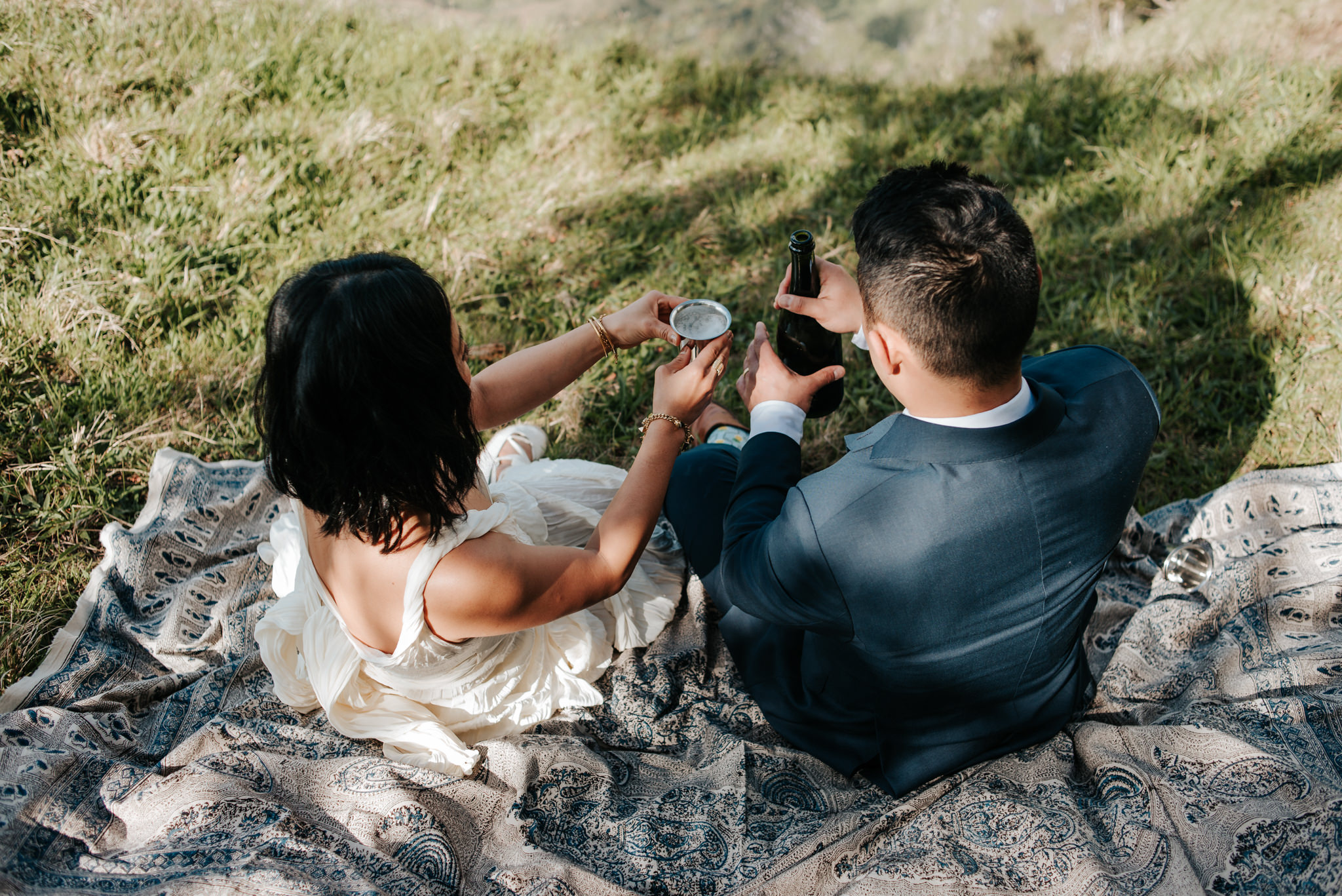 bride and groom toasting champagne on picnic blanket