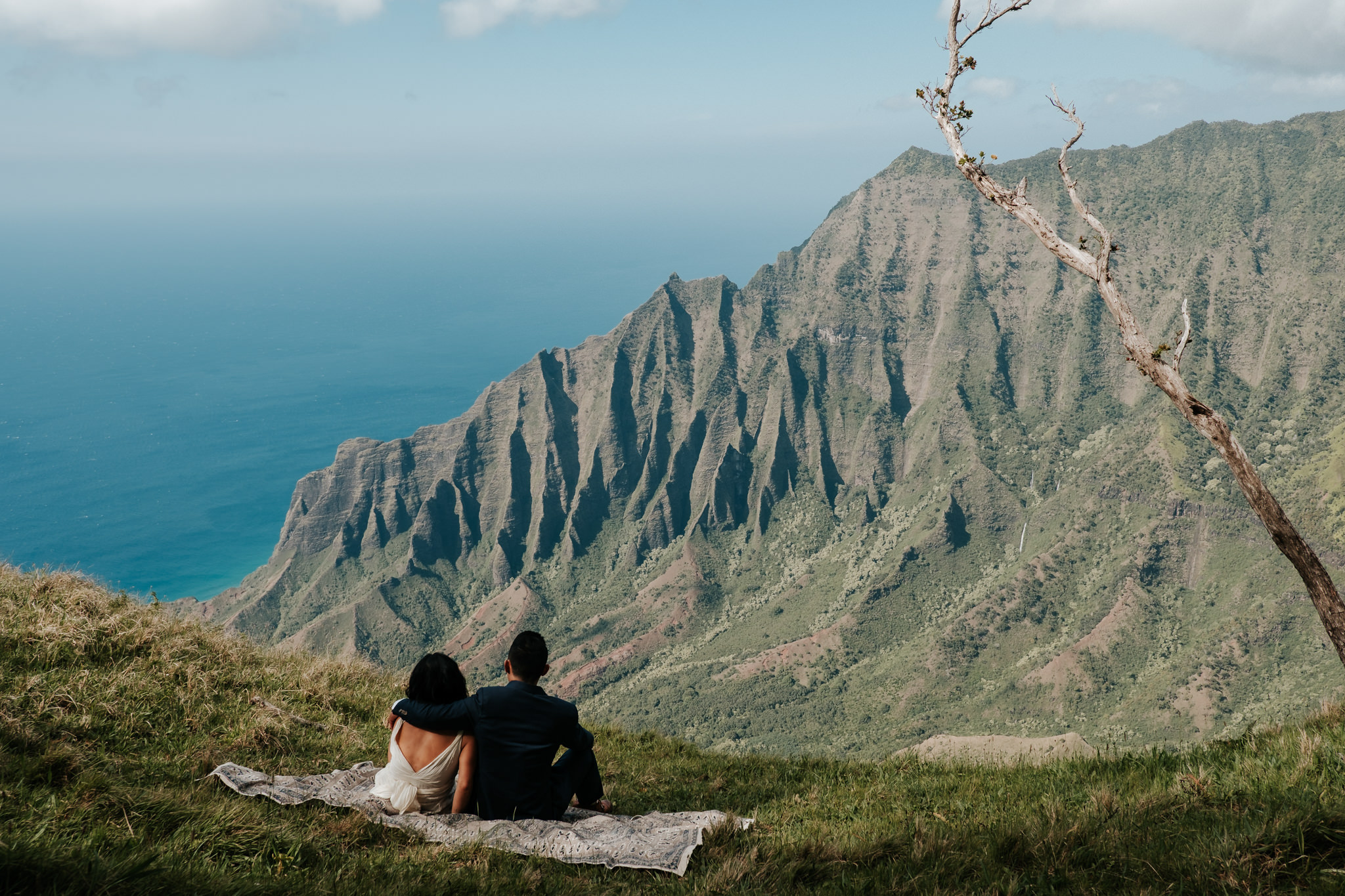 bride and groom sitting on blanket with view of Na pali Coast Kauai