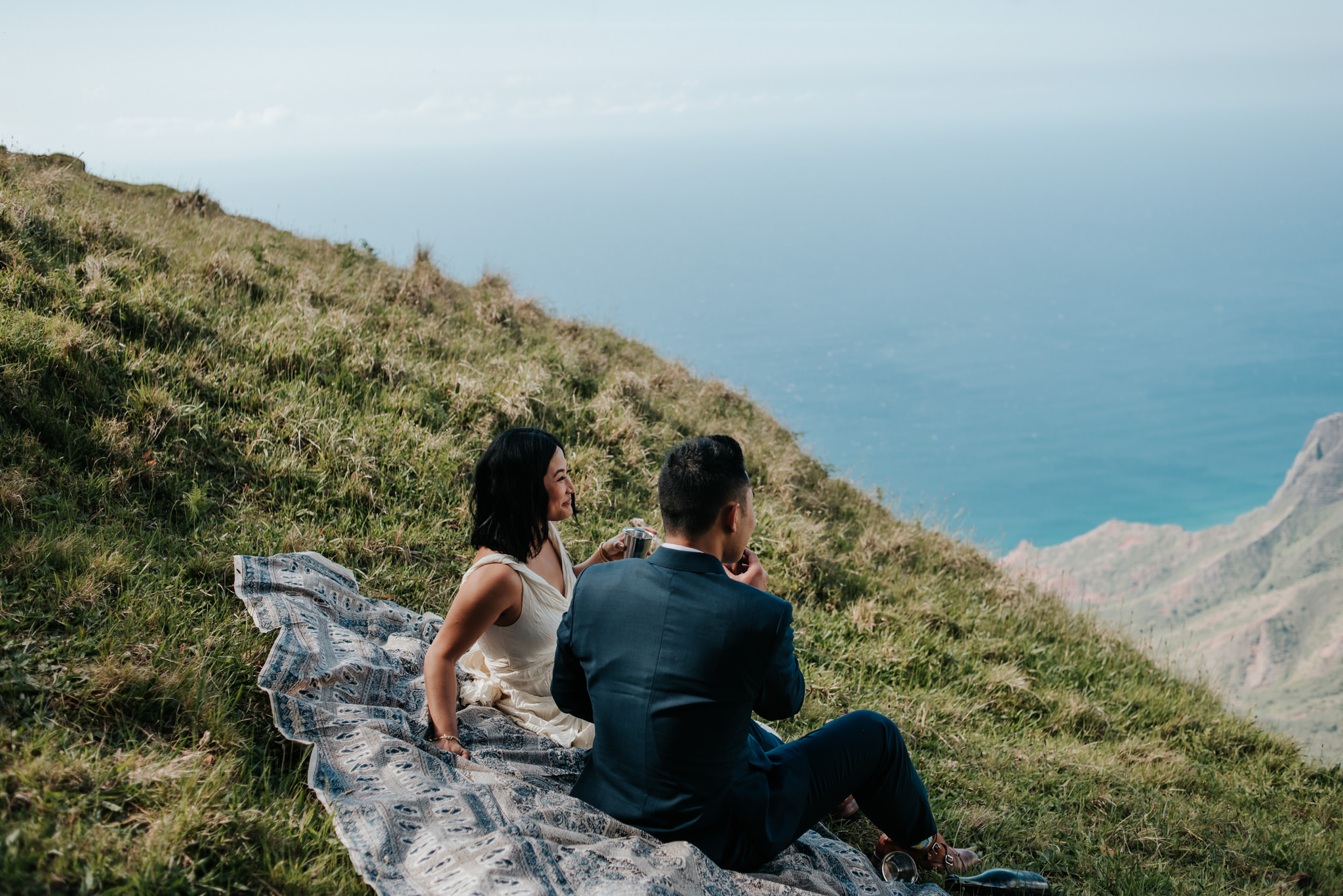 bride and groom toasting champagne on picnic blanket with view of Na pali Coast