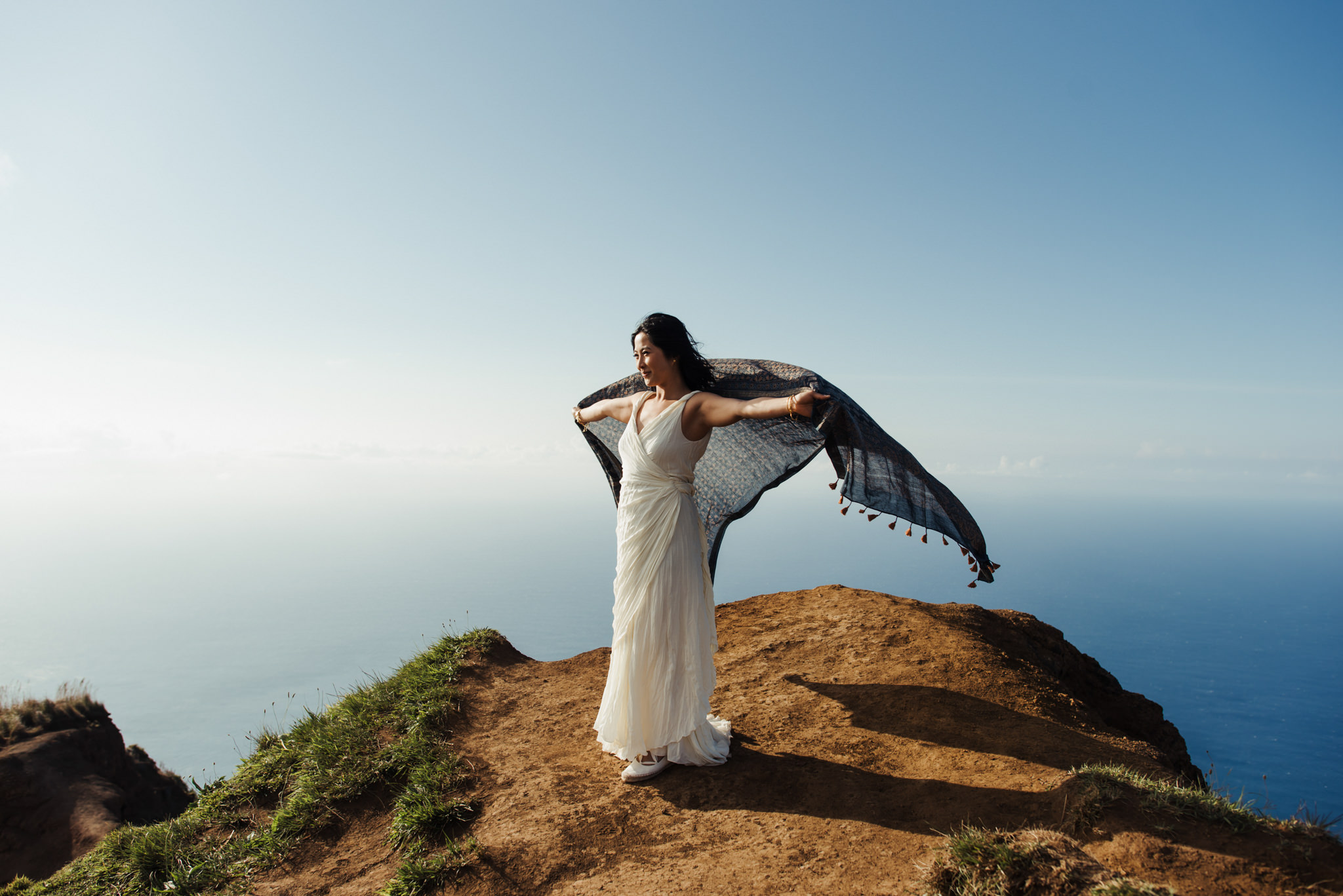 bride holding up scarf on edge of cliff as it floats in wind