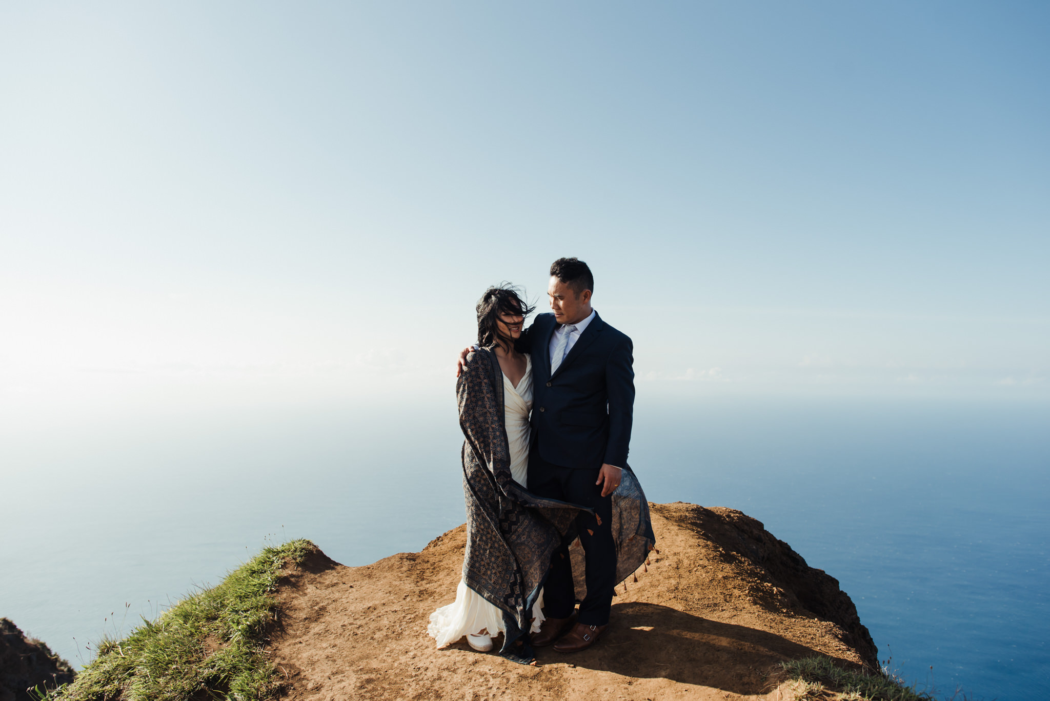 bride wrapped up in scarf on edge of cliff in Kauai