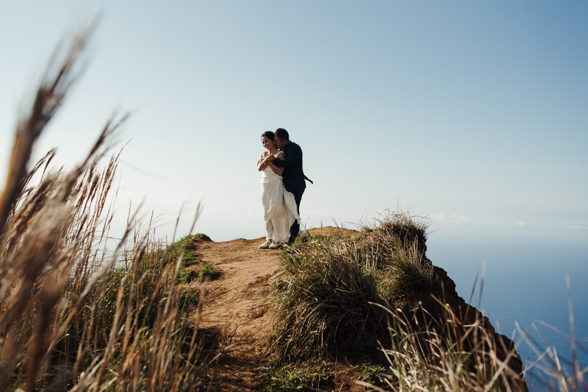 Bride and groom hugging on edge of cliff at top of Na Pali coast in Kokee State Park