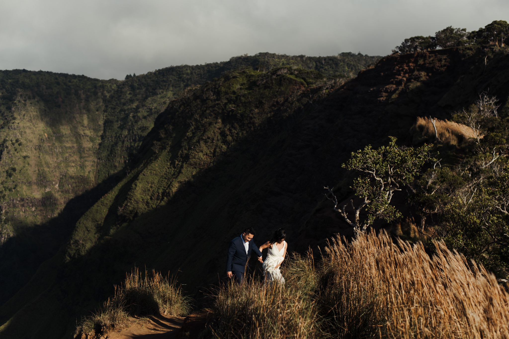 Bride and groom hiking up cliff side in Kokee State Park in Kauai