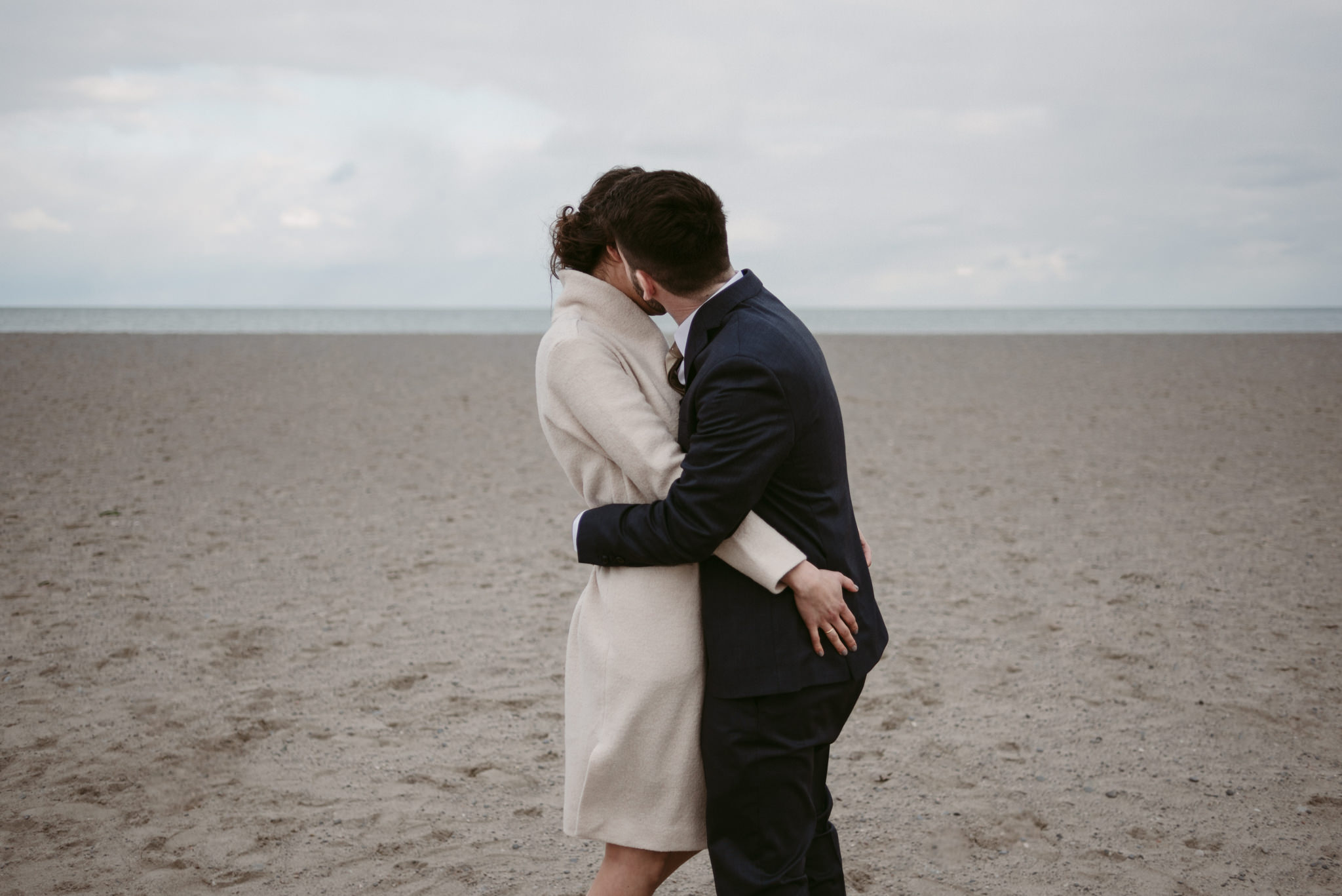 Bride and groom hugging and kissing in cold on the beach