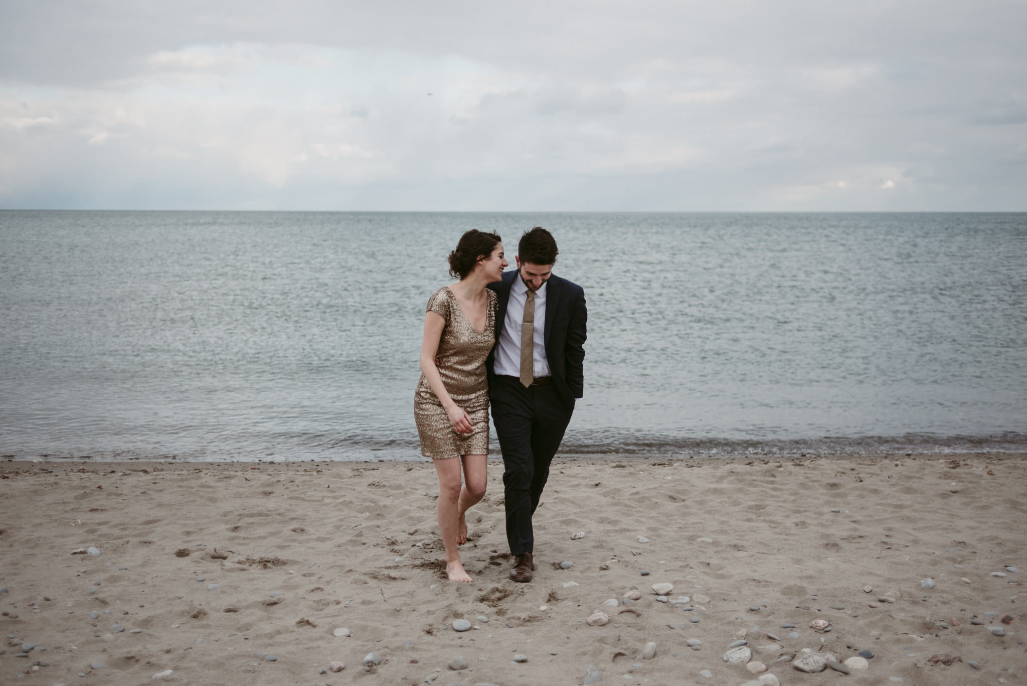 Woman in sequin dress and guy in suit laughing and walking on the beach