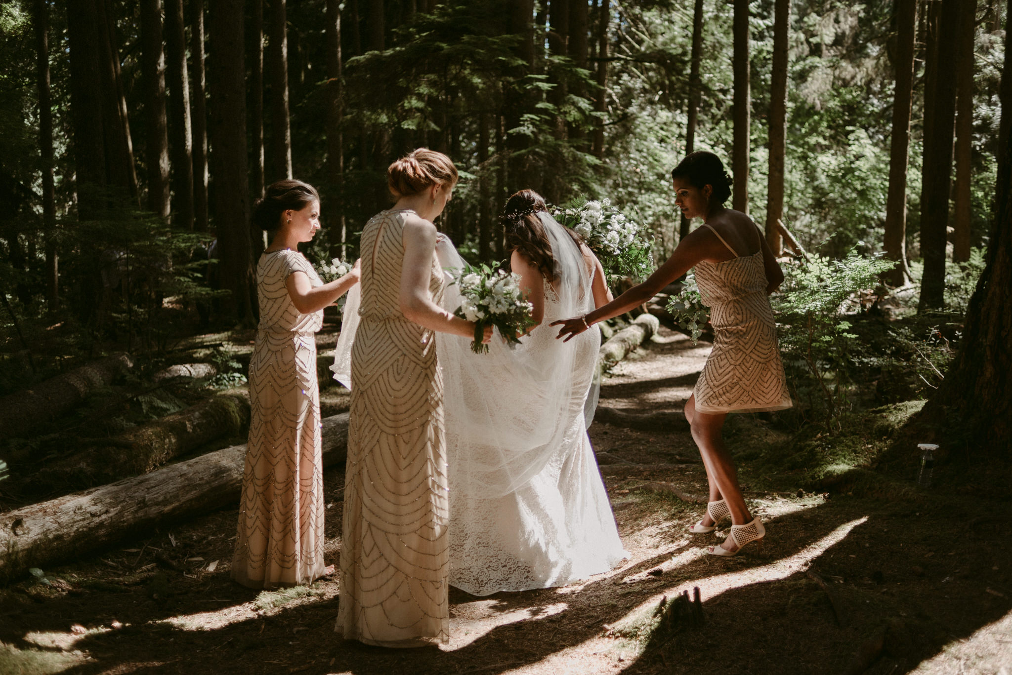 bridesmaids helping bride with dress in forest