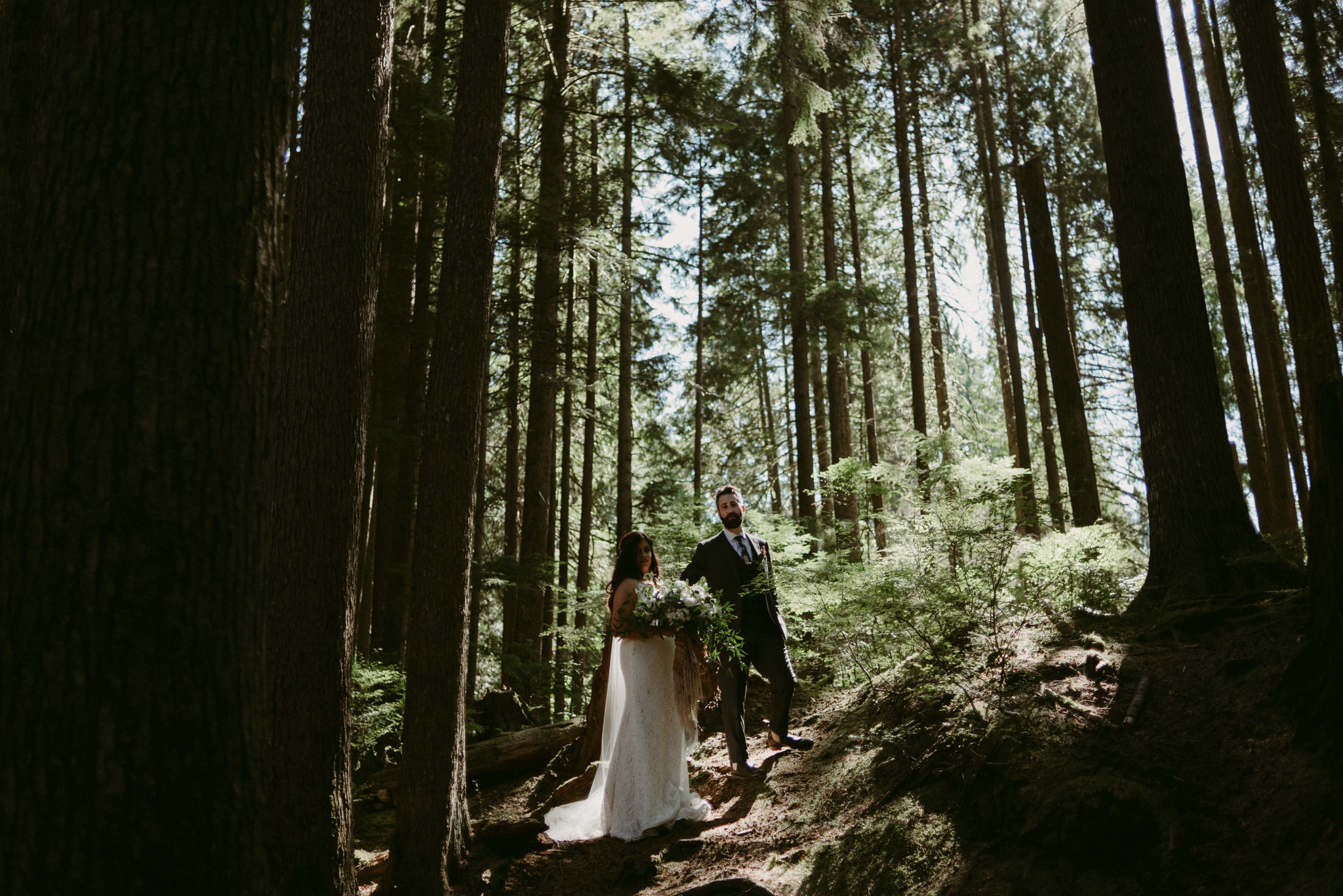 bride and groom standing in light in forest of tall pines