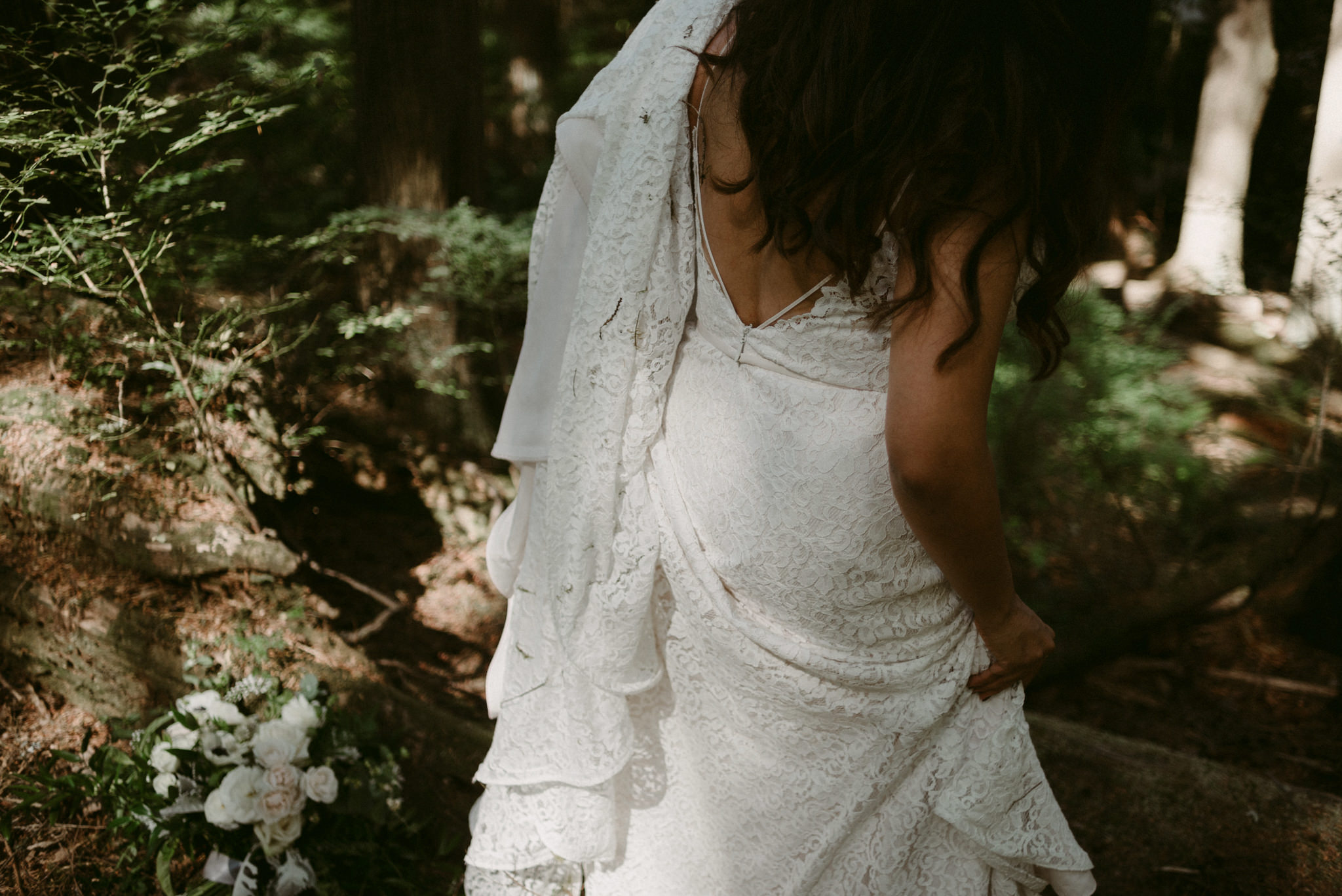 bride walking while holding dress in forest