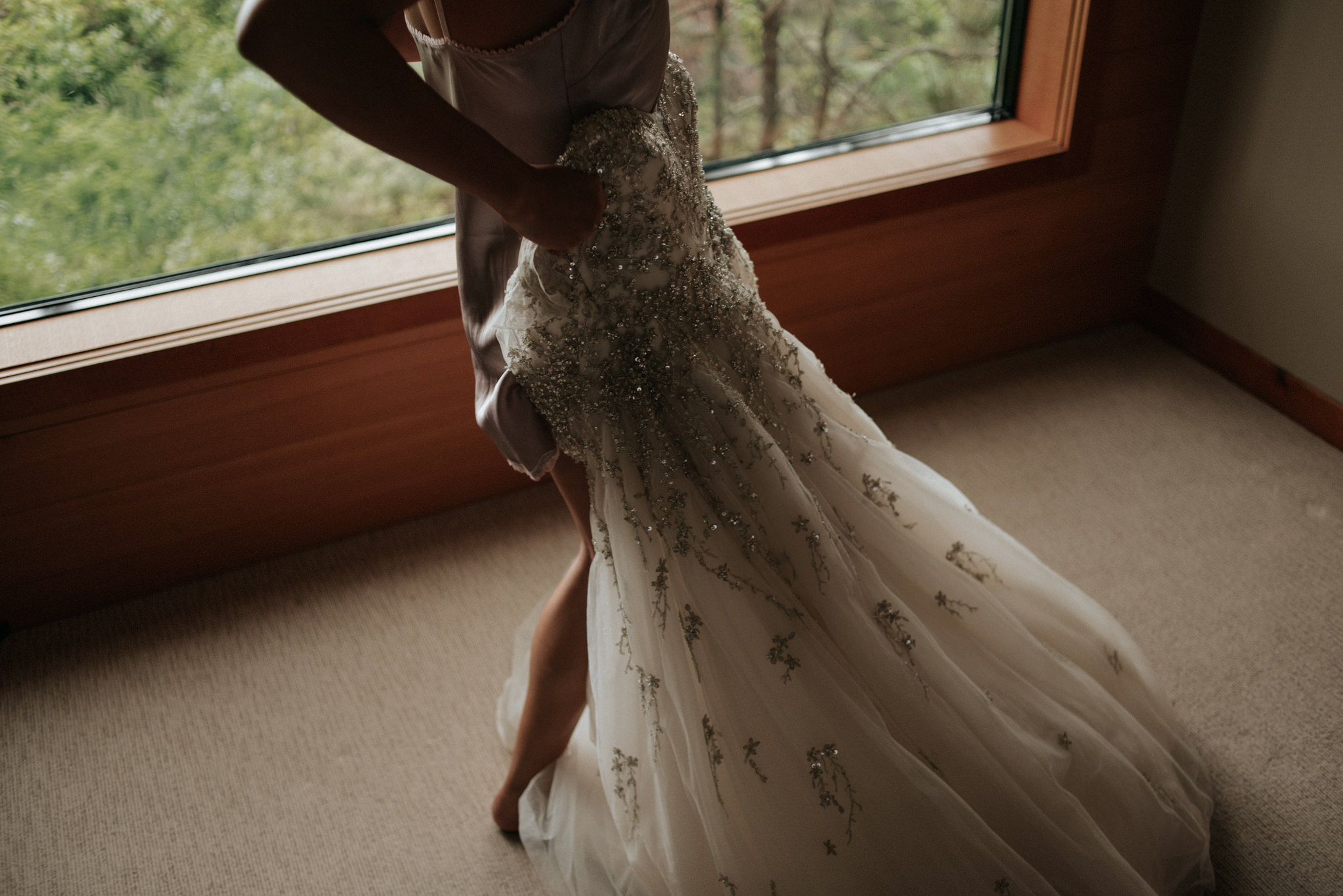 bride stepping into dress by window at Wickaninnish Inn for her Tofino Elopement