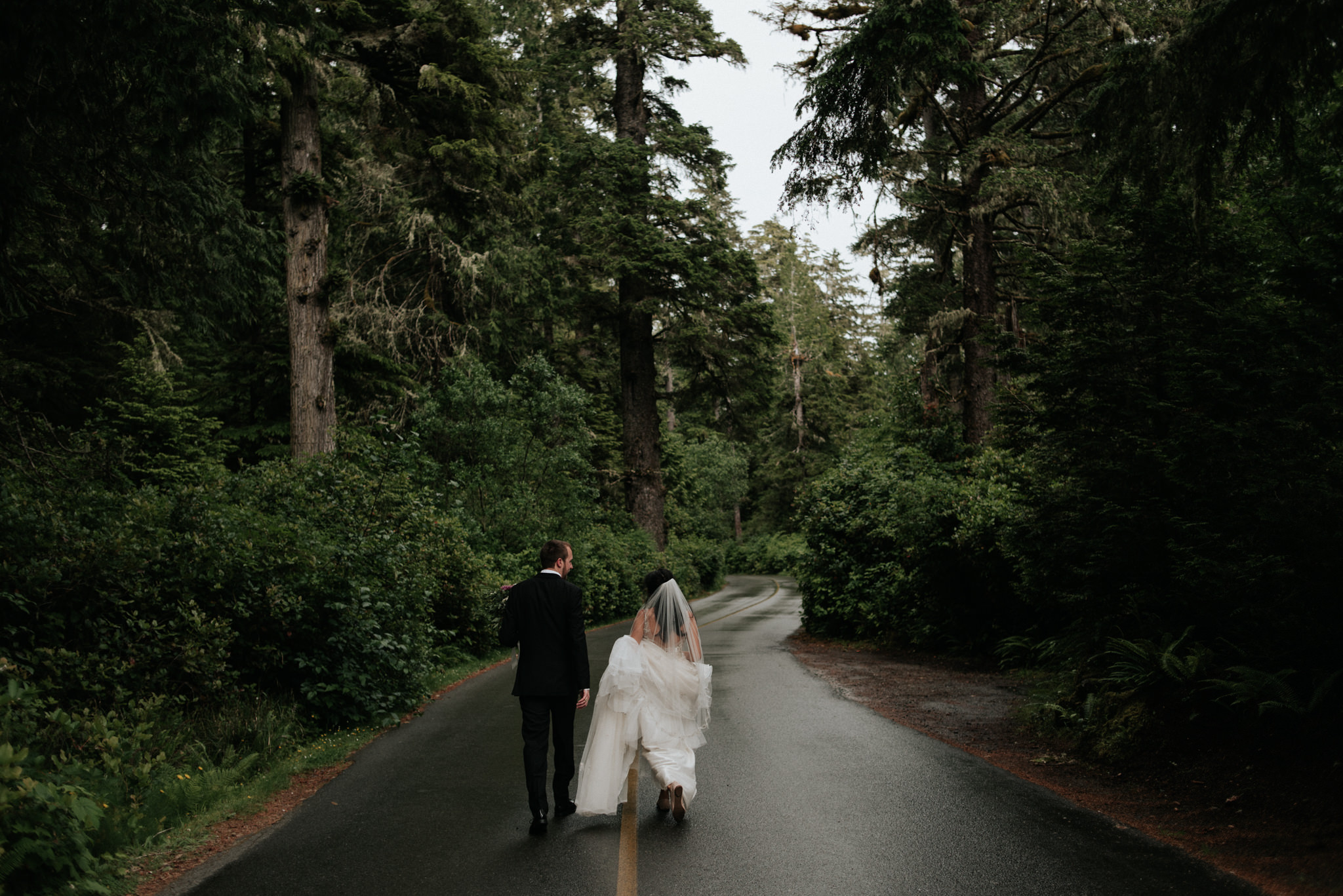 bride and groom walking down road surrounded by forest in Tofino