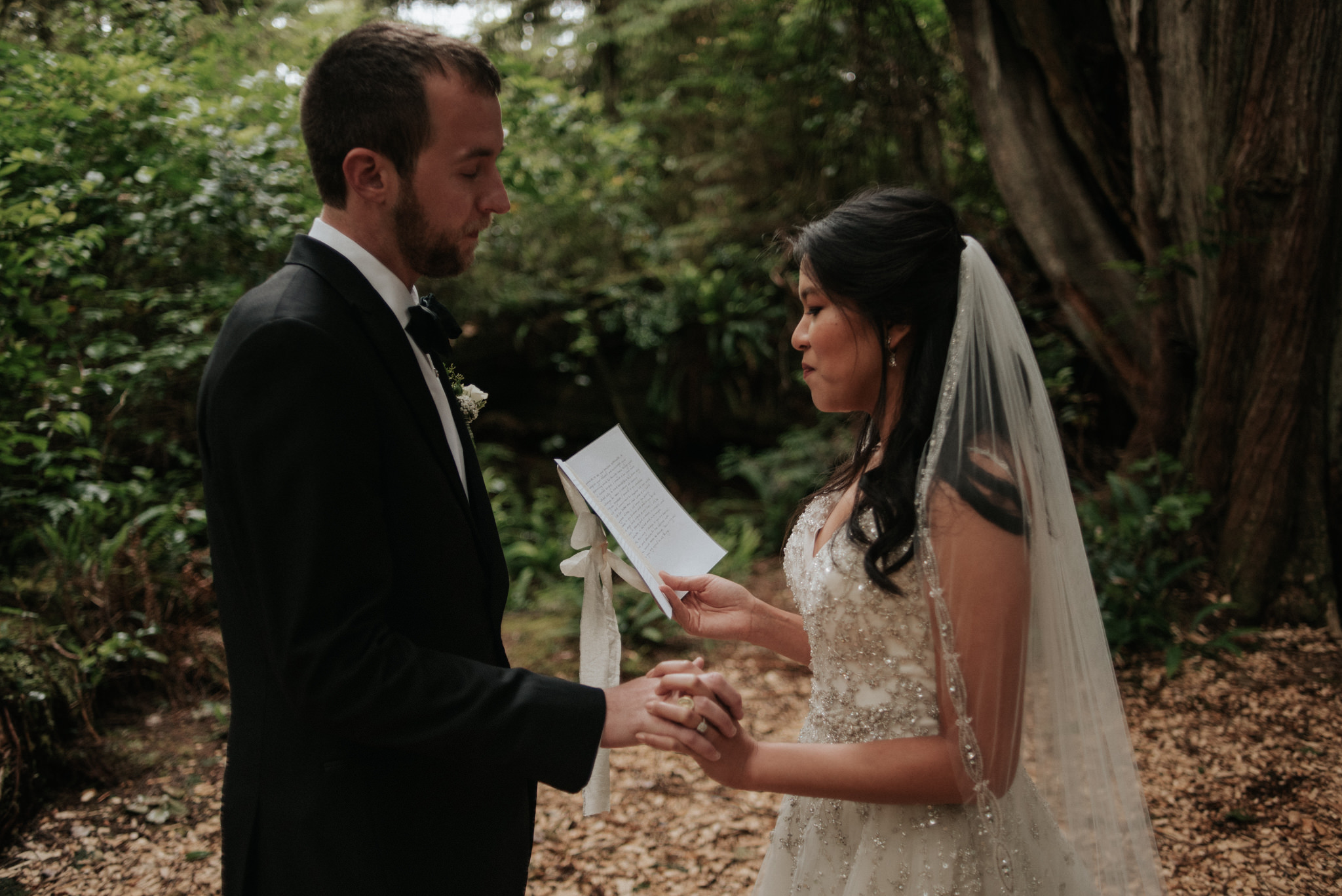 couple holding hands and reading vows to each other in forest for intimate elopement in Tofino