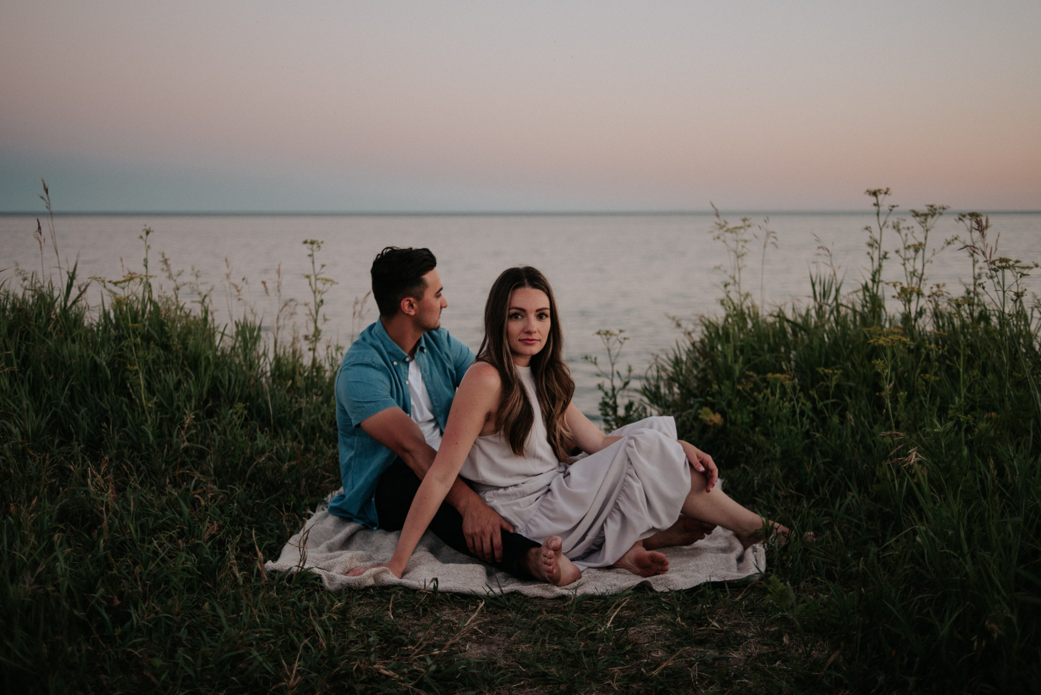 couple lying down on ground on blanket by the lake at sunset