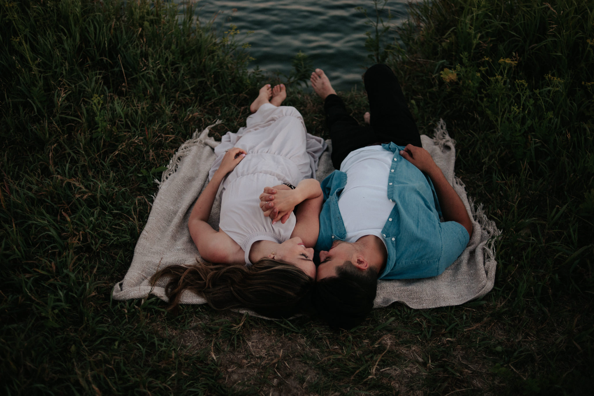 couple lying down on ground on blanket by the lake at sunset