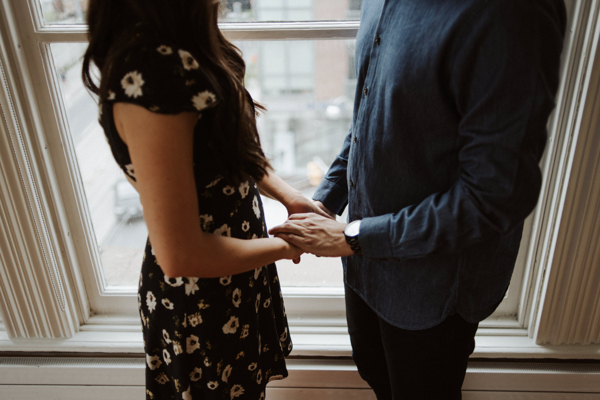 couple facing each other holding hands in front of window in home