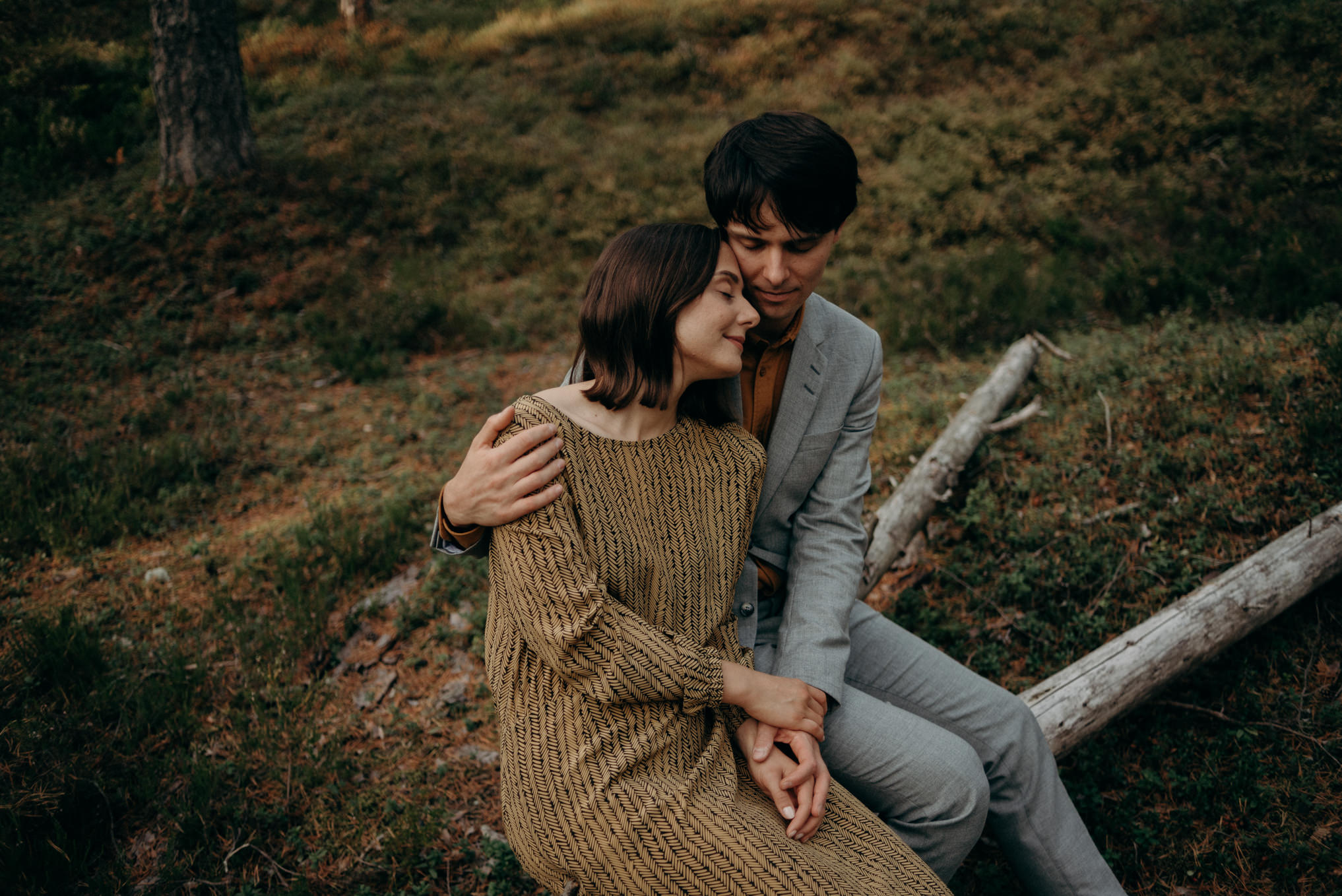 young couple sitting on fallen tree in forest