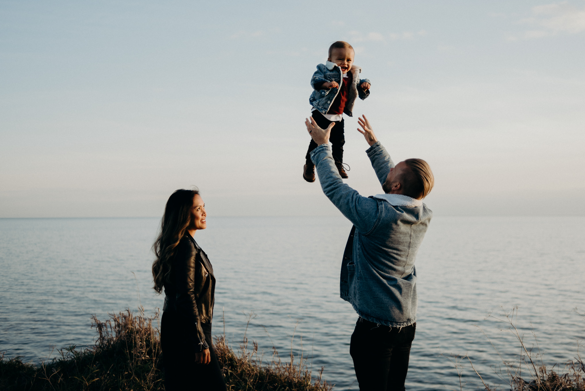 dad throwing little boy up in the air at sunset by the lake