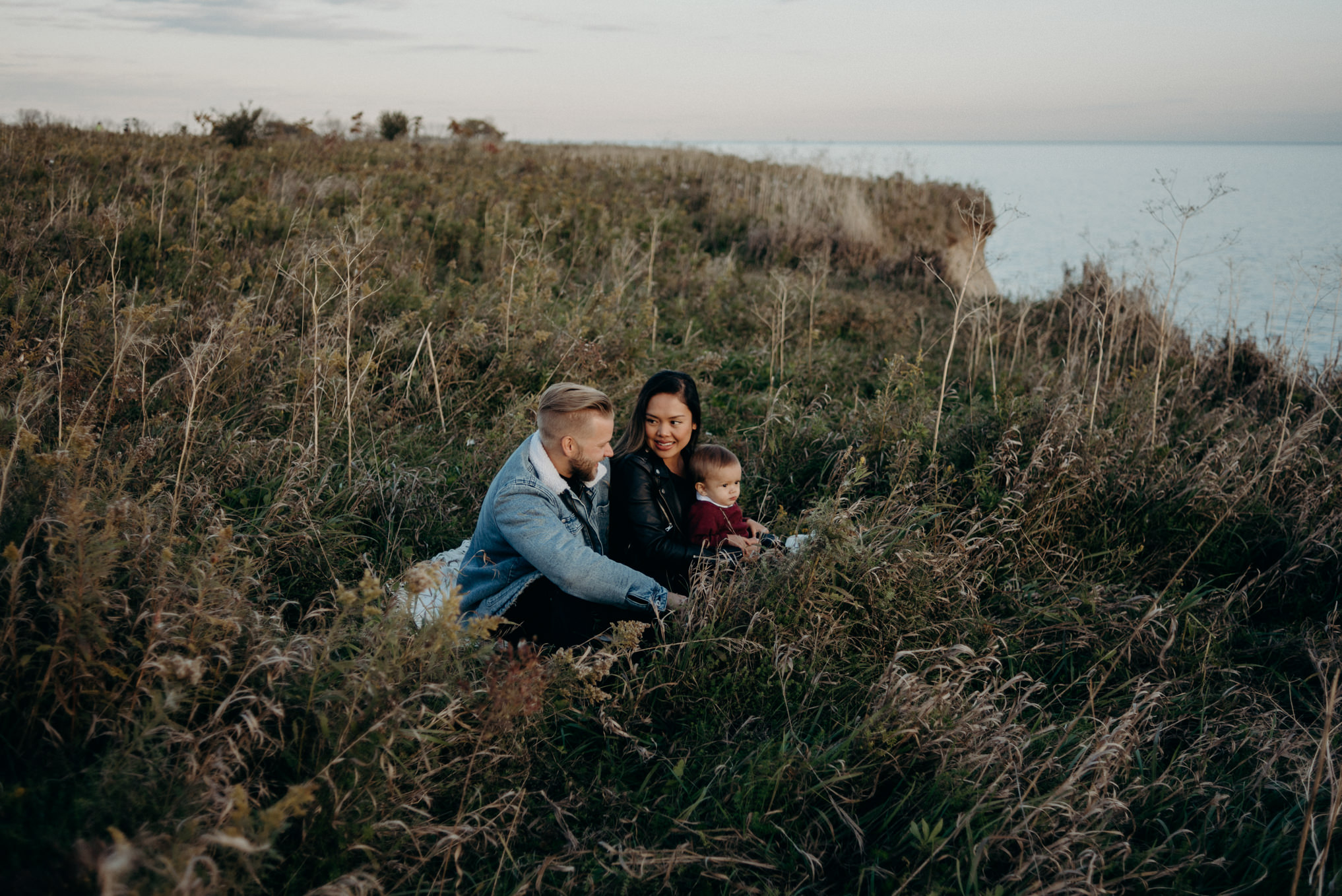 young hip couple sitting in grass by lake at sunset