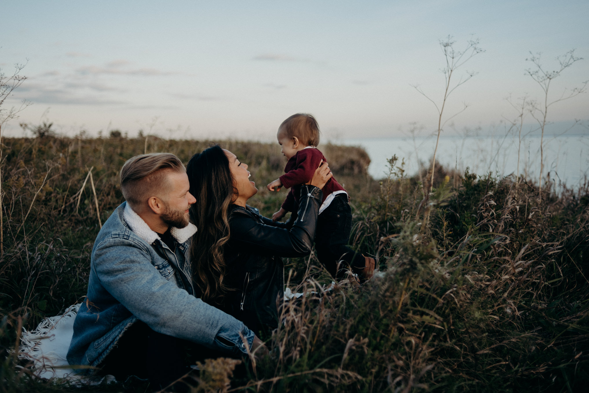 young hip couple sitting in grass playing with baby