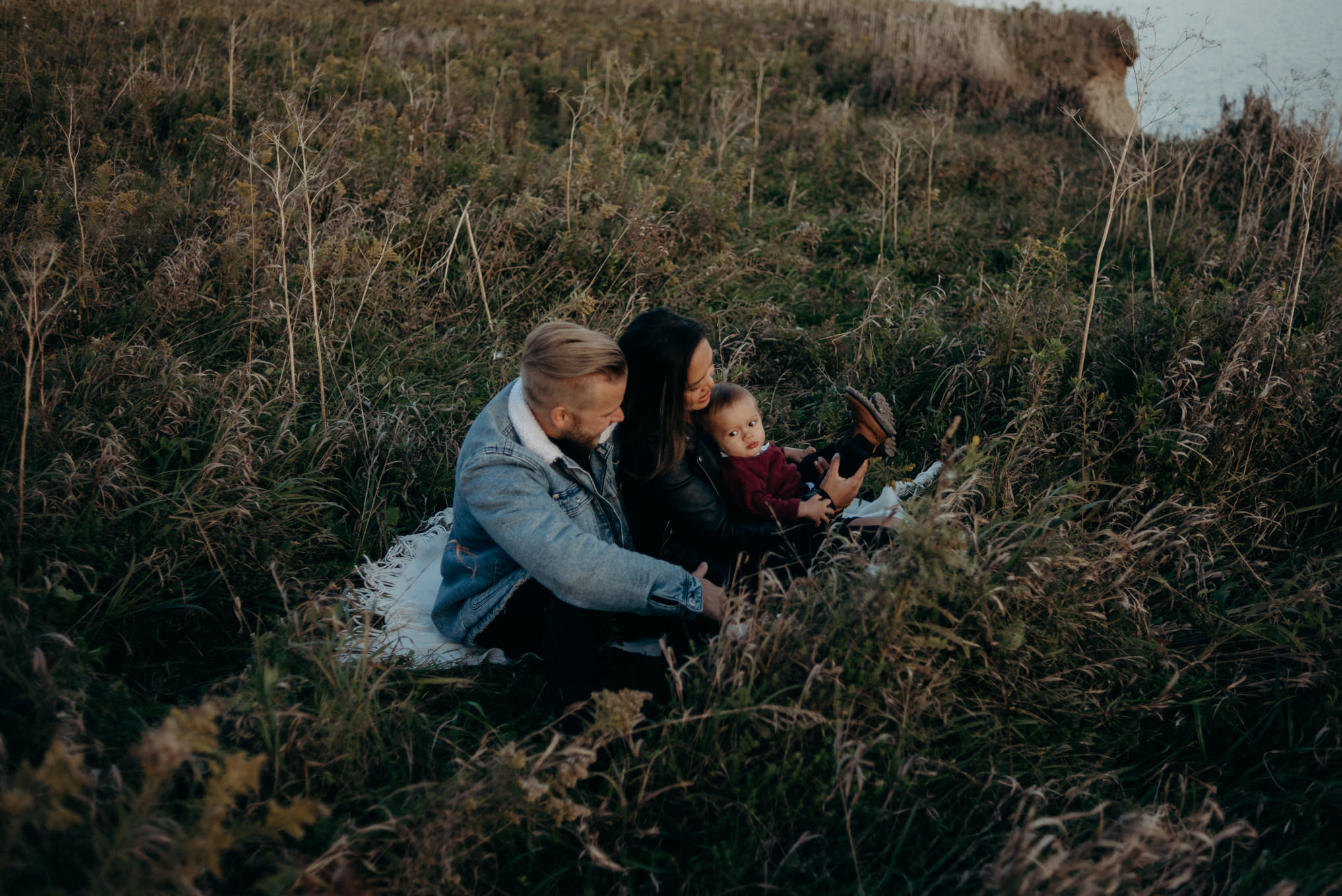 young hip couple sitting in grass playing with baby