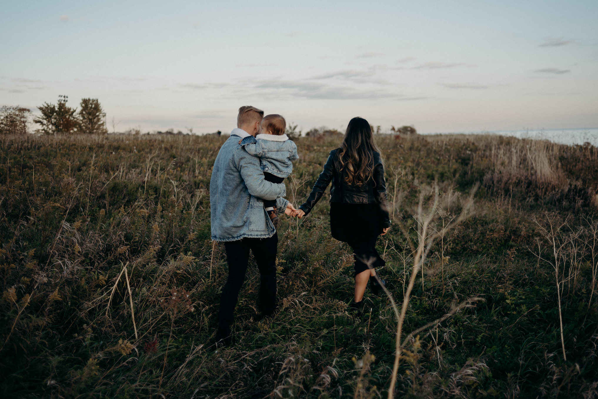 young couple holding hands and carrying baby boy by lake