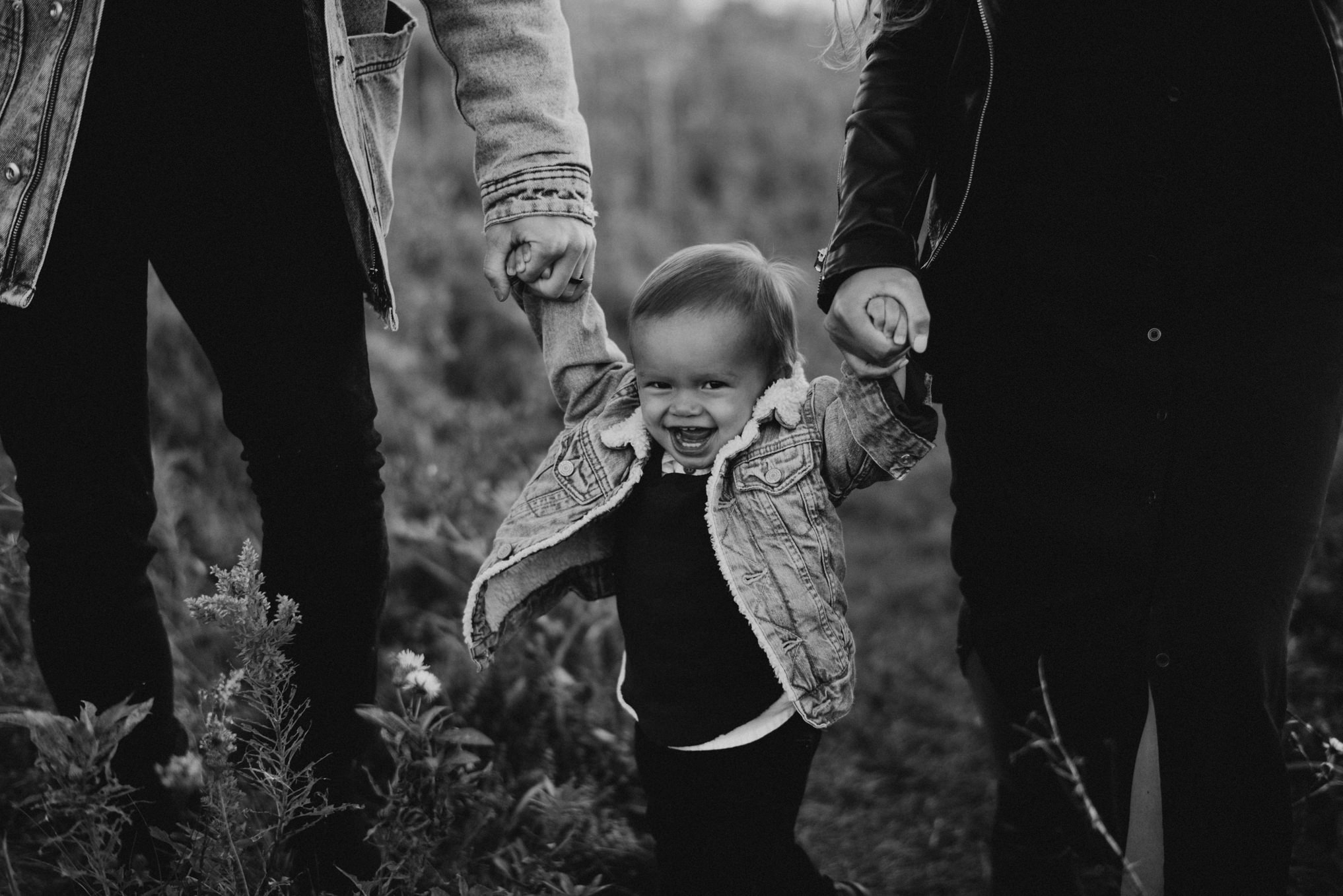 baby boy smiling at camera while holding mom and dads hands