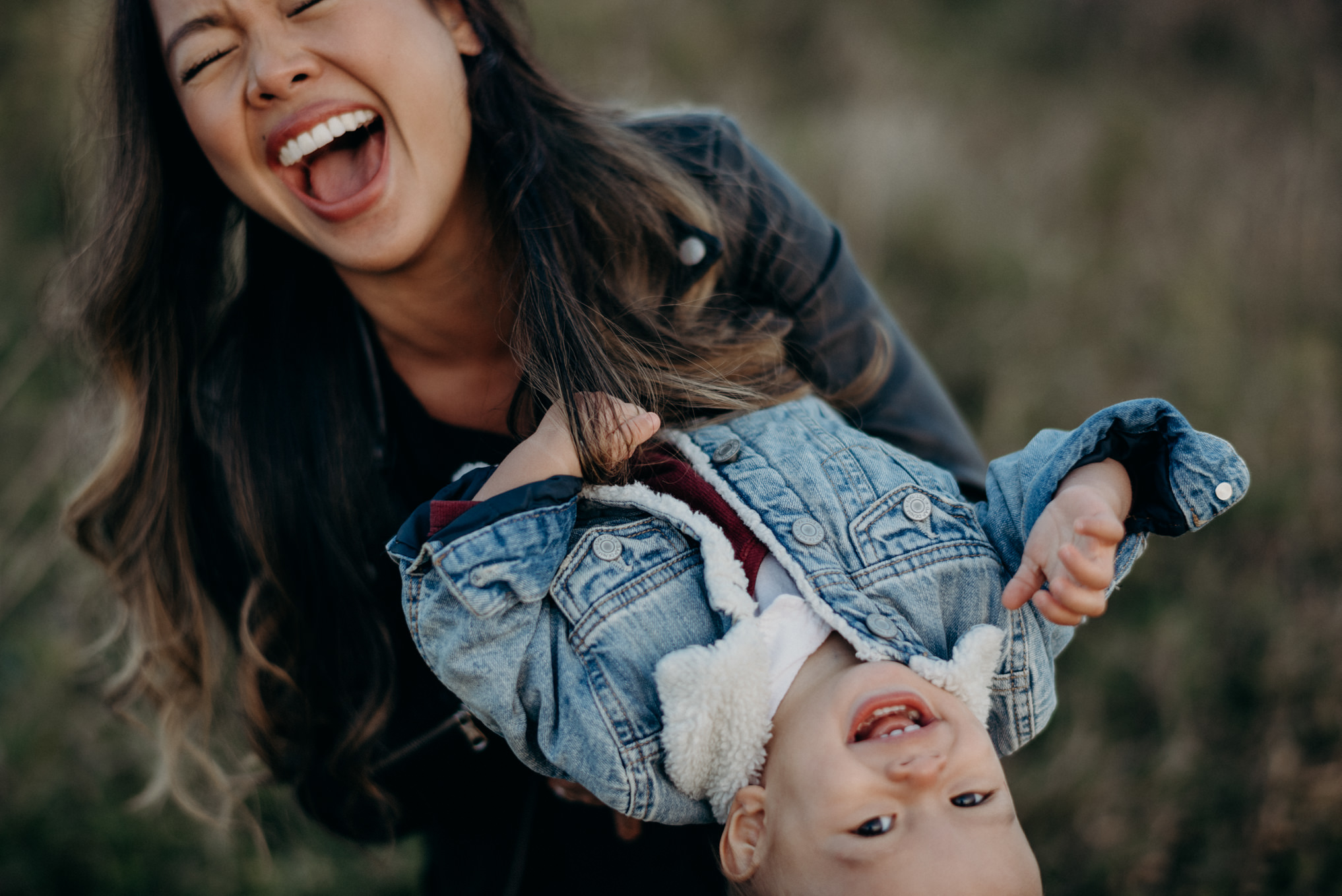 mom laughing while holding baby boy outside