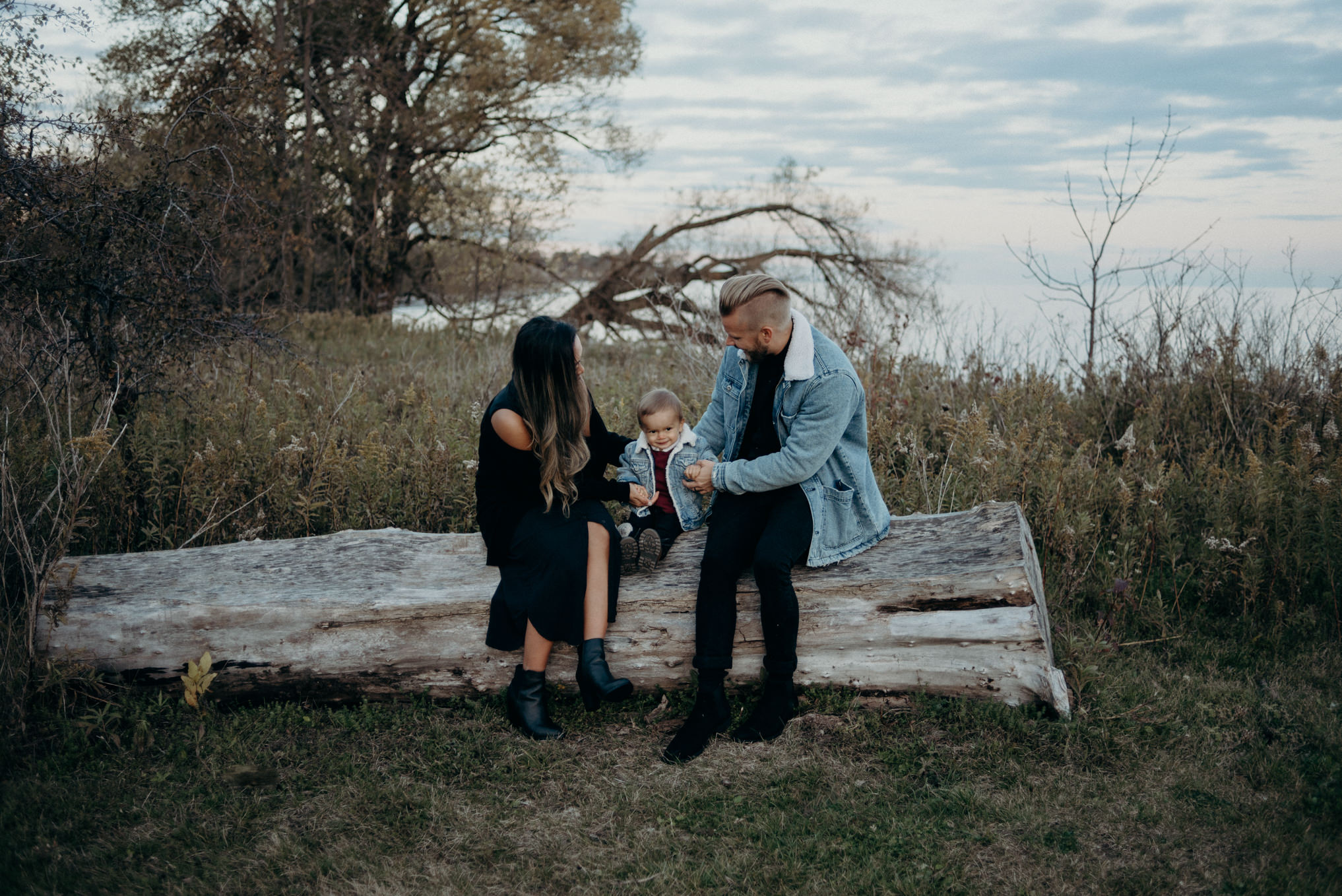 dad holding baby boy in matching jean jacket outside by water