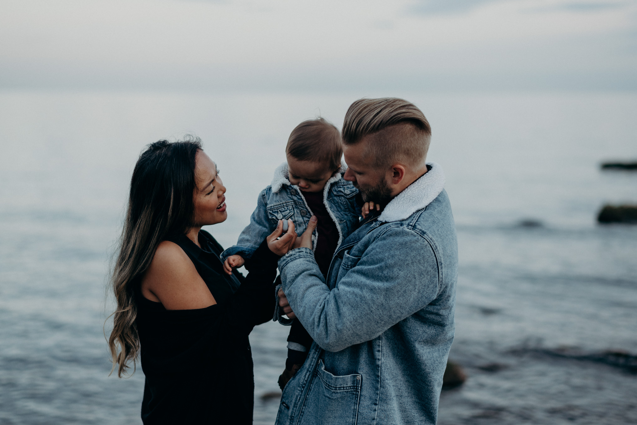 dad throwing baby boy in air with matching jean jacket while mom watches