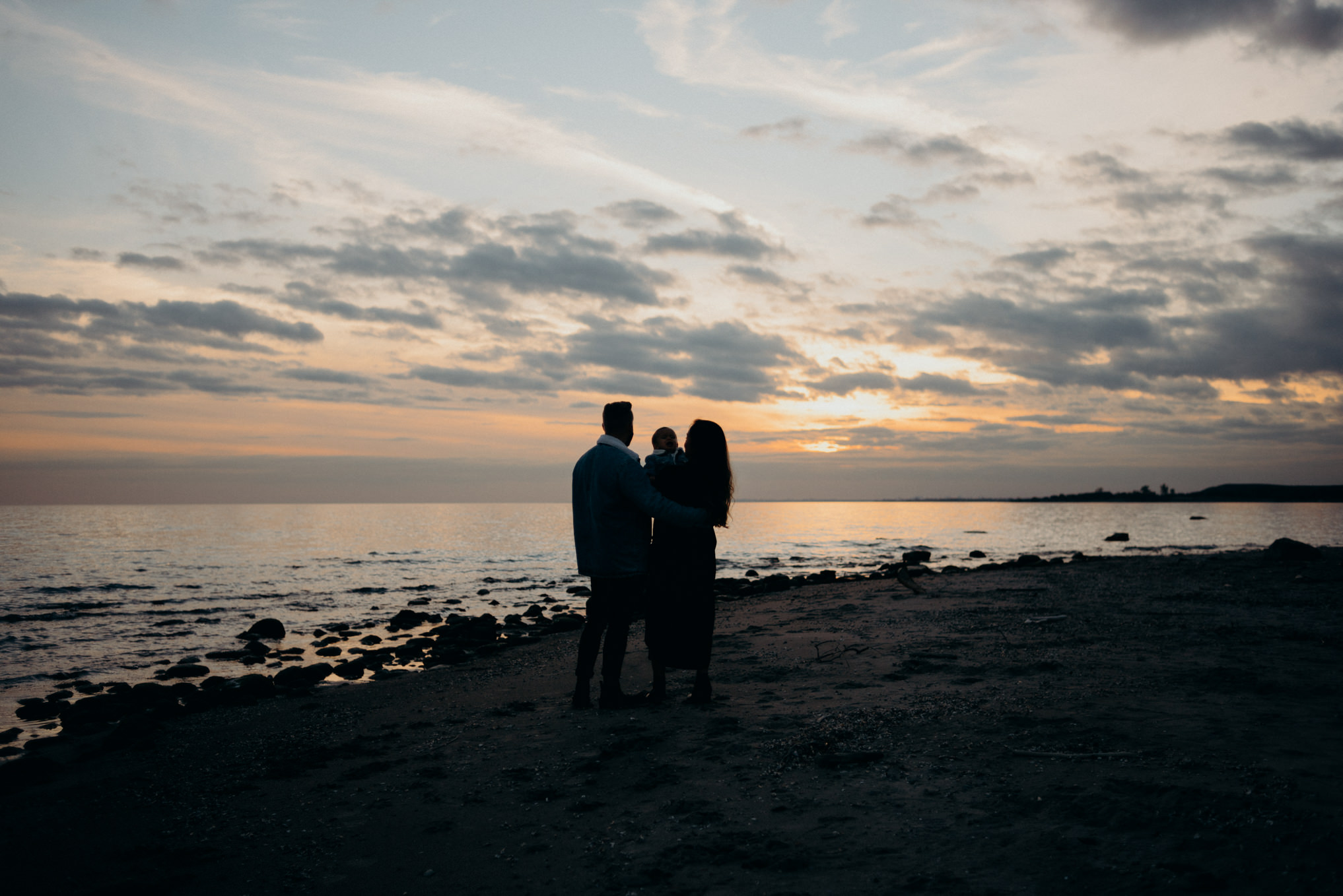 Portrait of young family watching sunset on the beach in Toronto