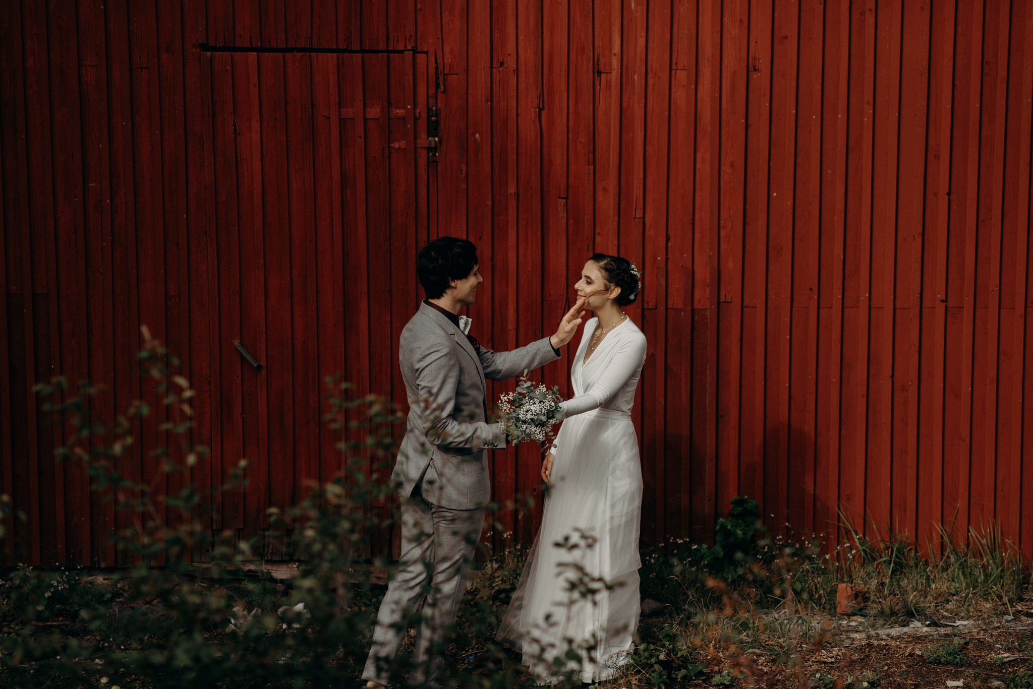 Groom removing hair from brides face in front of red barn wall