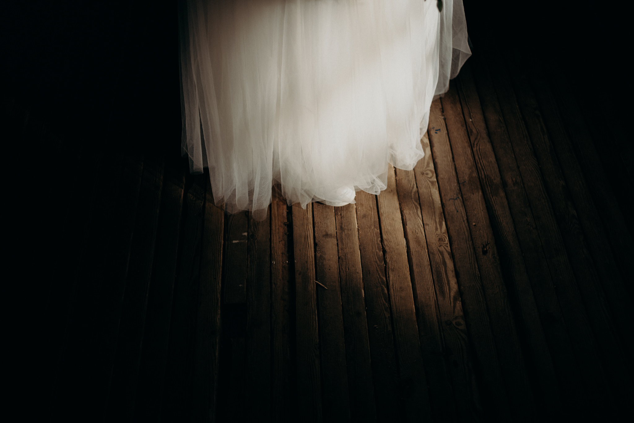 groom kissing bride in sunlight coming through windows of old boathouse surrounded by old sails