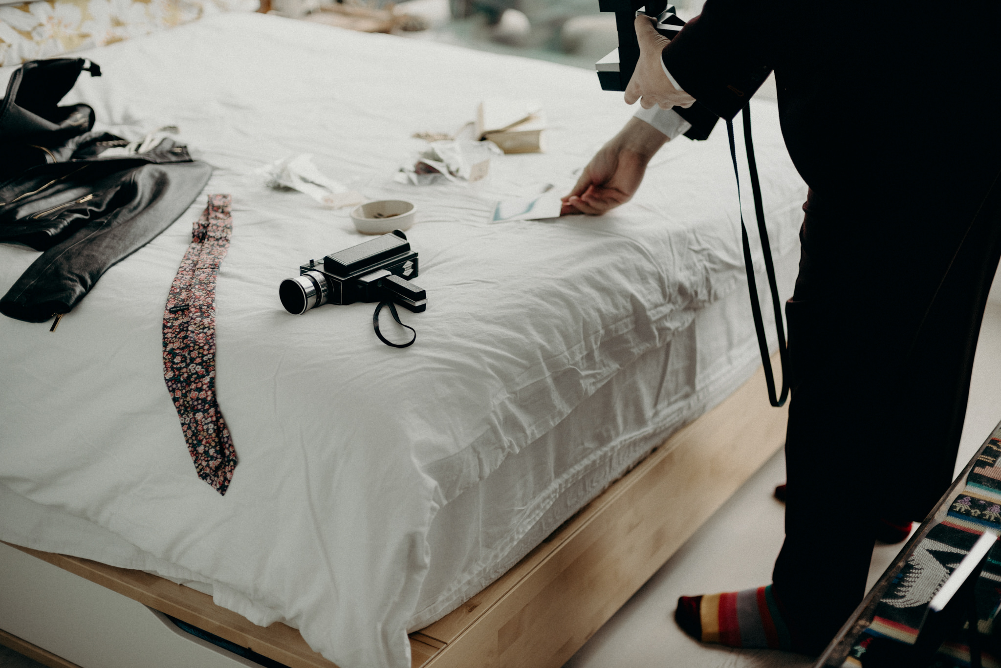 groom takin polaroid of bride getting ready in condo bedroom with large windows